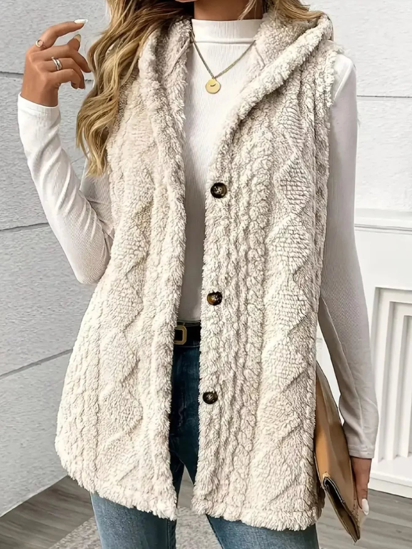 Woman wearing cozy beige cable knit button-up sherpa vest with hood over white long sleeve top and jeans