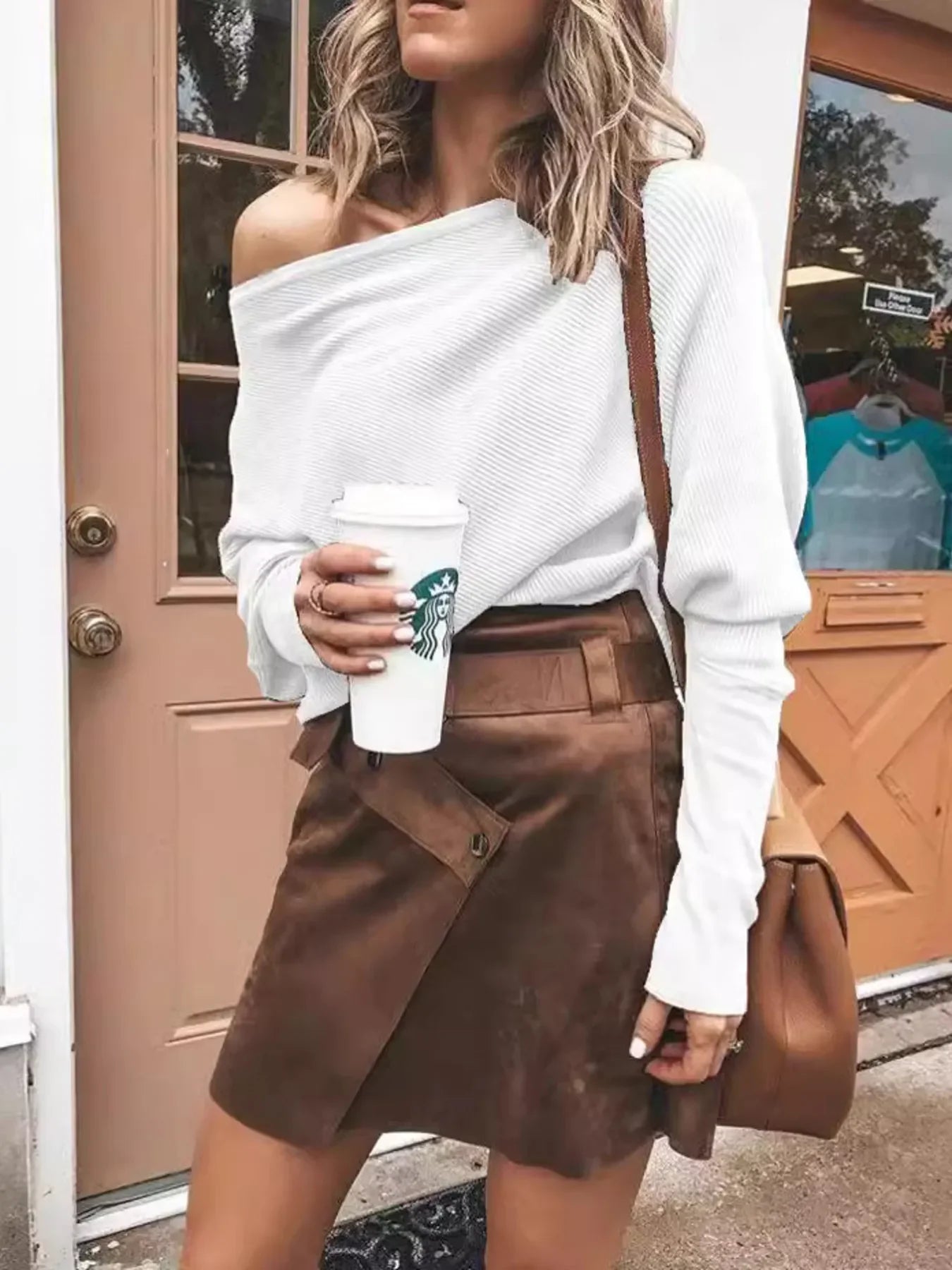 Woman in white off-shoulder sweater and brown suede skirt holding Starbucks coffee cup