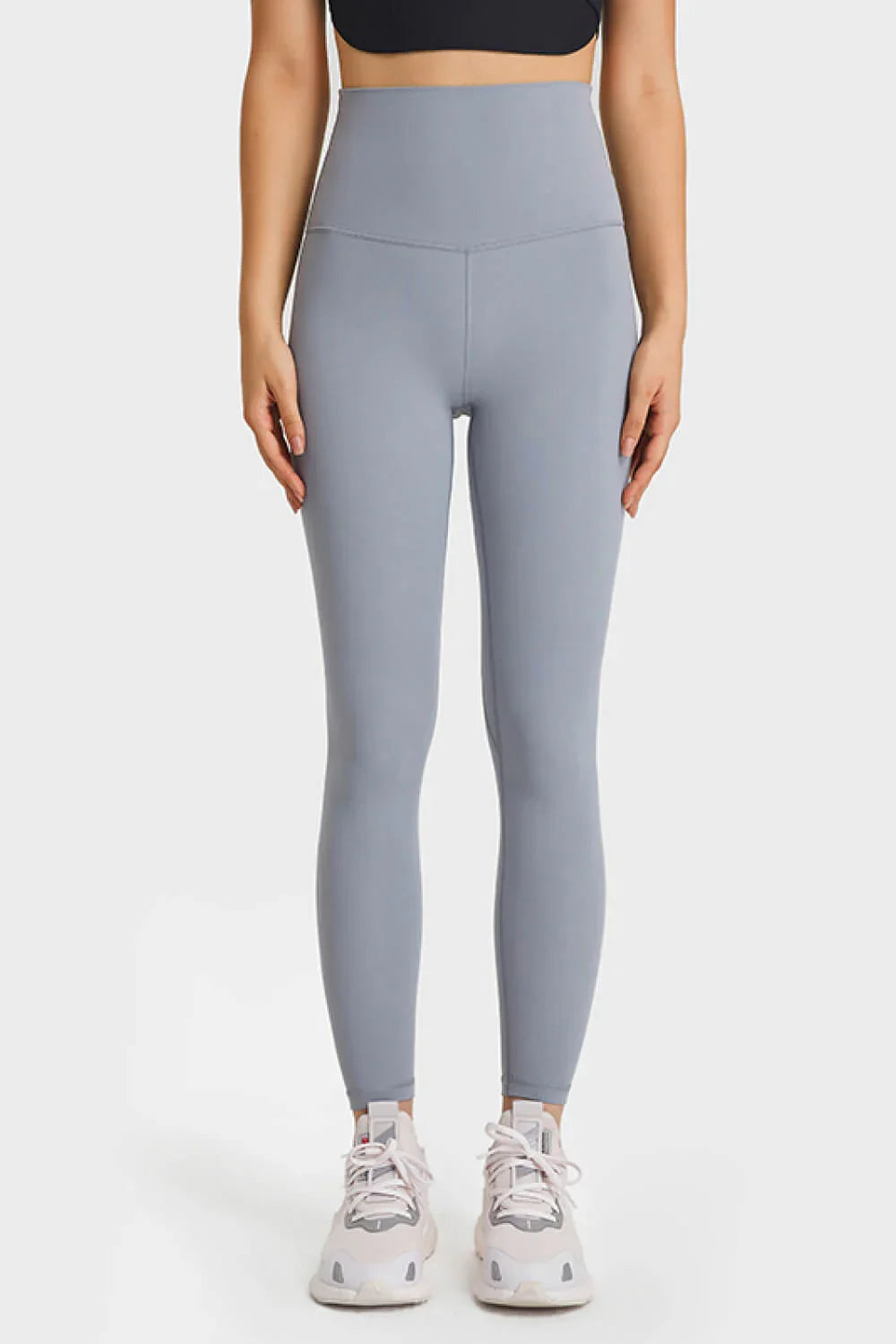Front view of woman wearing high-waisted grey leggings and white athletic sneakers