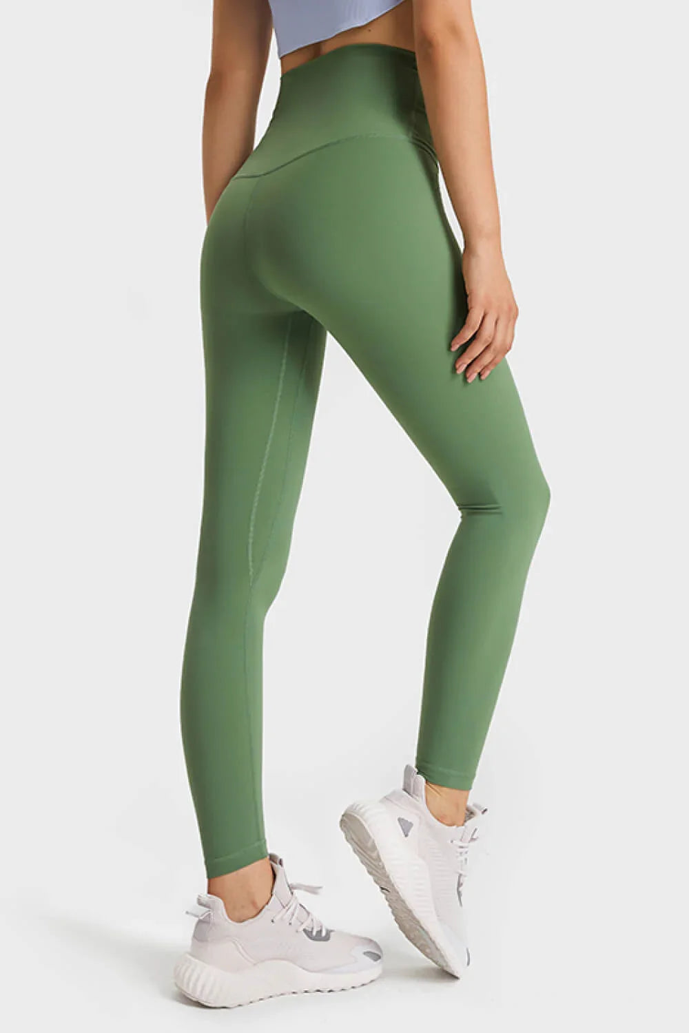 Woman wearing high-waisted olive green leggings and white athletic sneakers on white background
