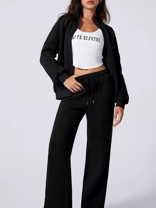 Woman wearing black zip-up jacket and wide-leg pants with white crop top featuring black text