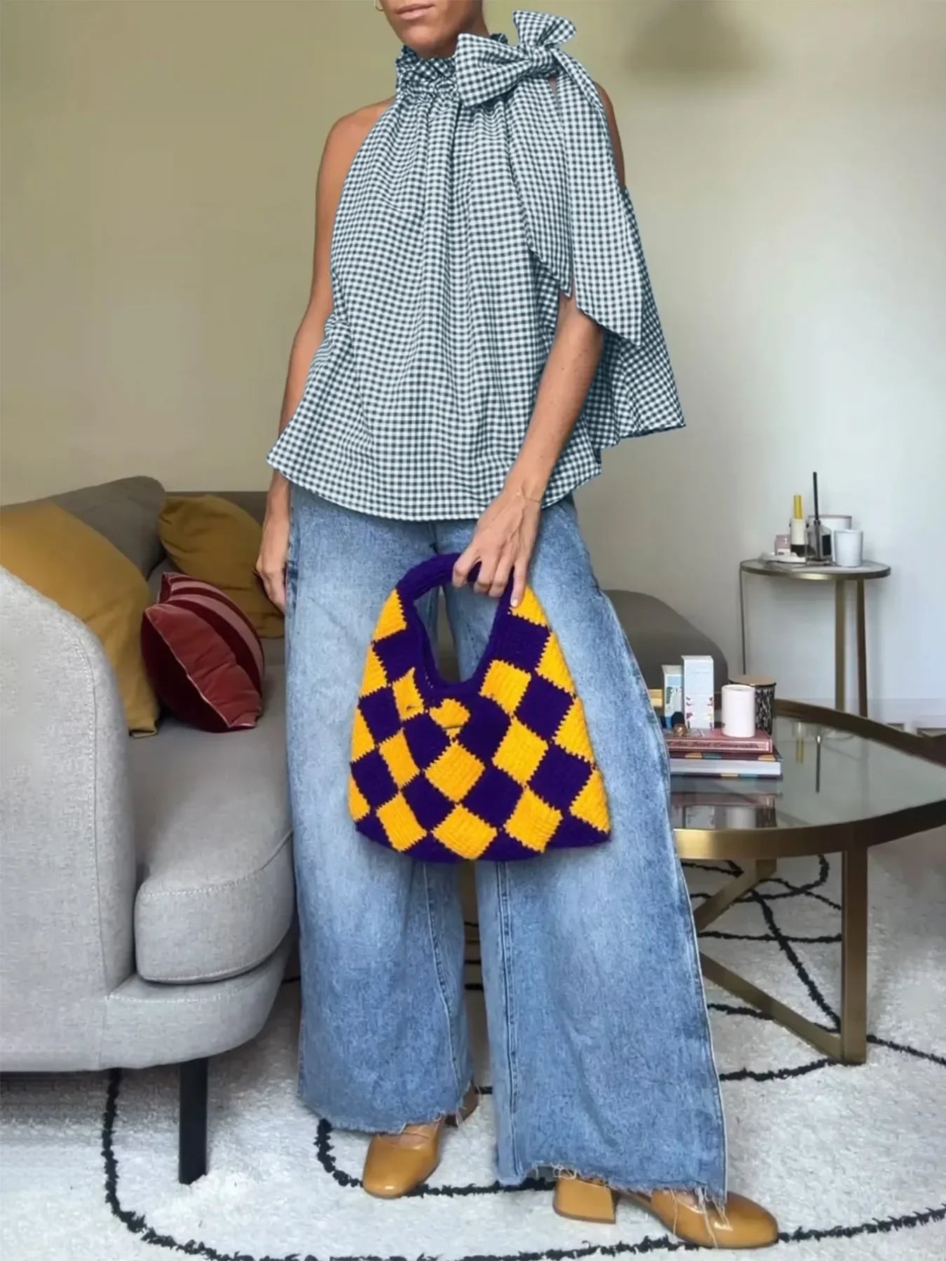 Woman in wide-leg jeans, gingham top, holding purple and yellow crochet bag