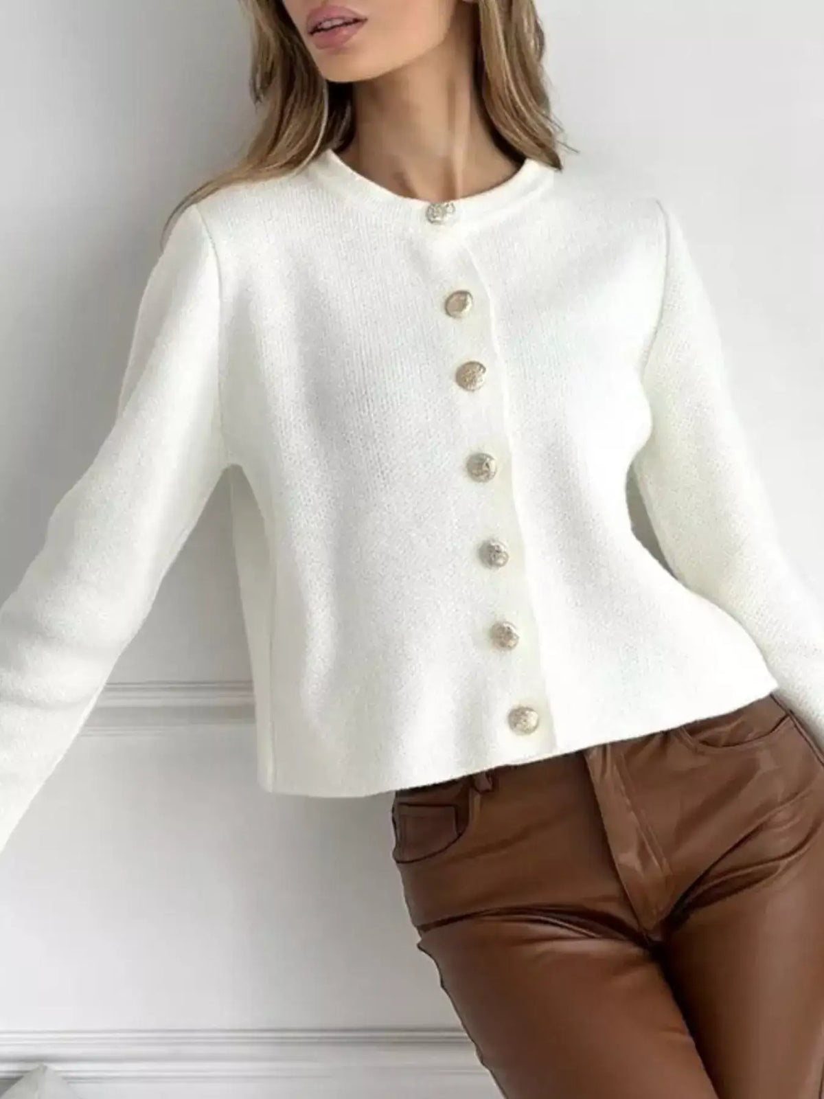 Woman wearing a white crew neck button down cardigan by Evie's Dreamland paired with brown faux leather pants.