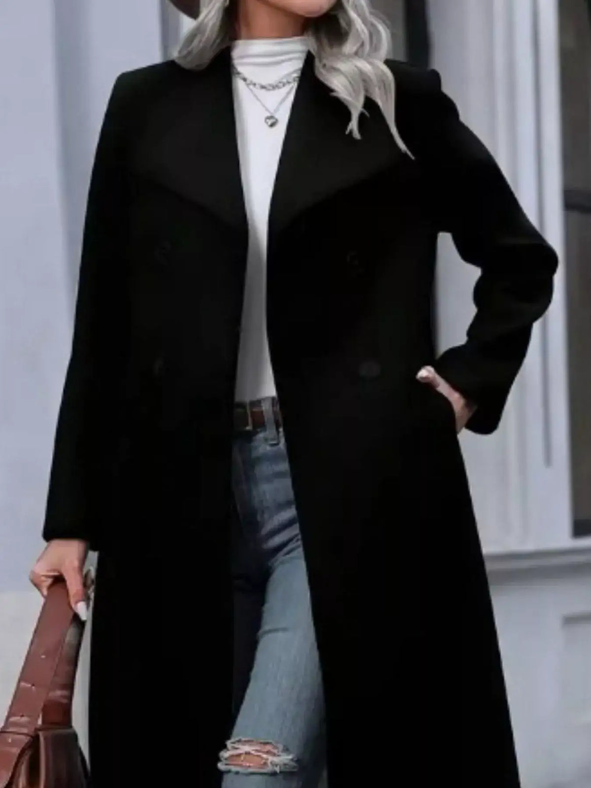 Woman wearing an Evie's Dreamland black double-breasted longline overcoat with a white top and blue jeans.