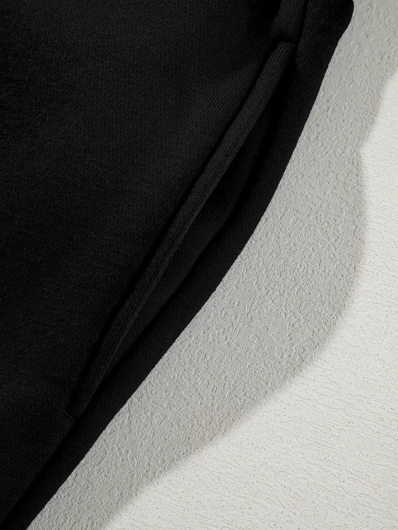 Close-up of black knit fabric with a folded edge on a textured white surface