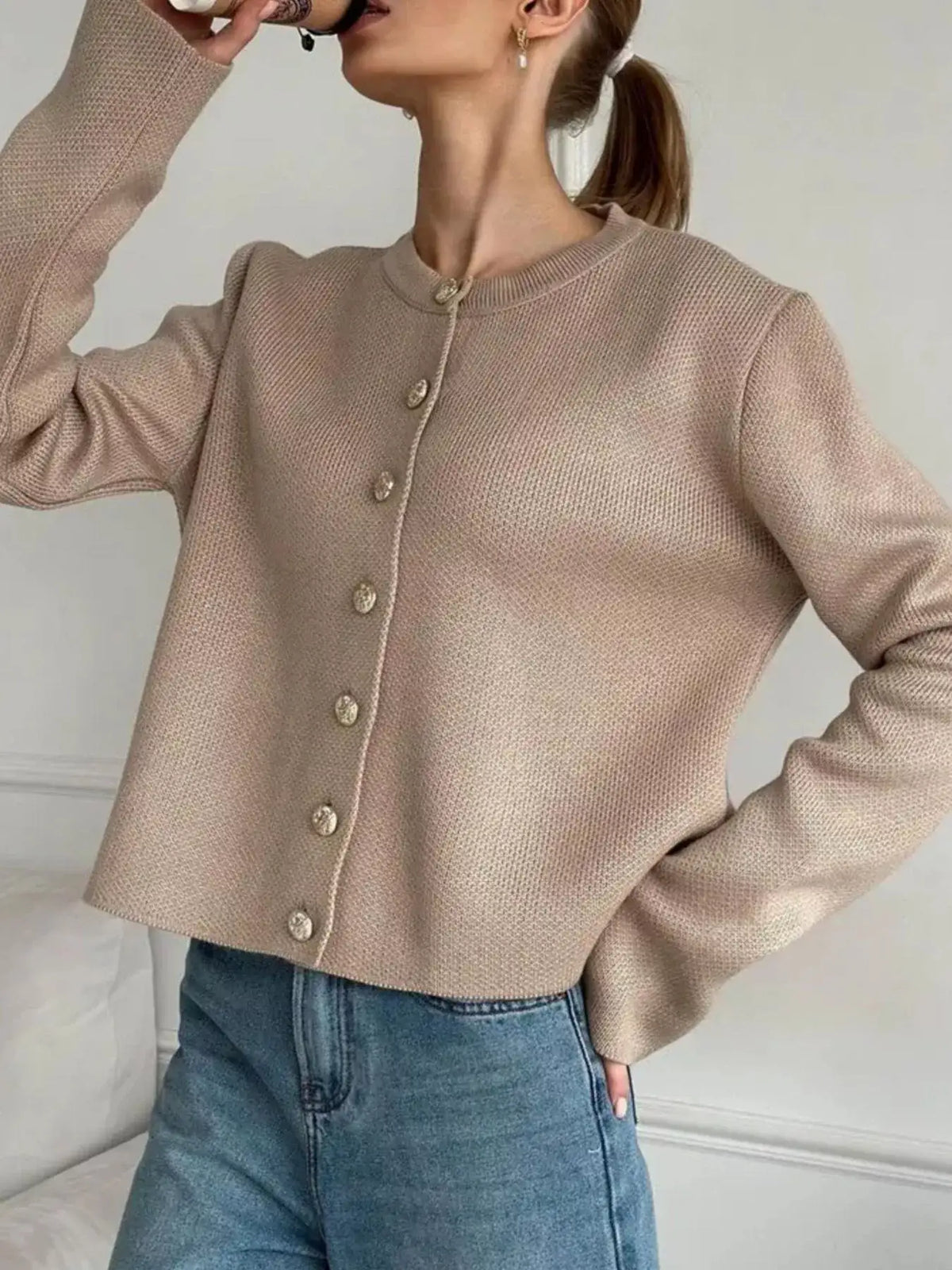 Woman wearing a beige crew neck button down cardigan by Evie's Dreamland paired with blue jeans.