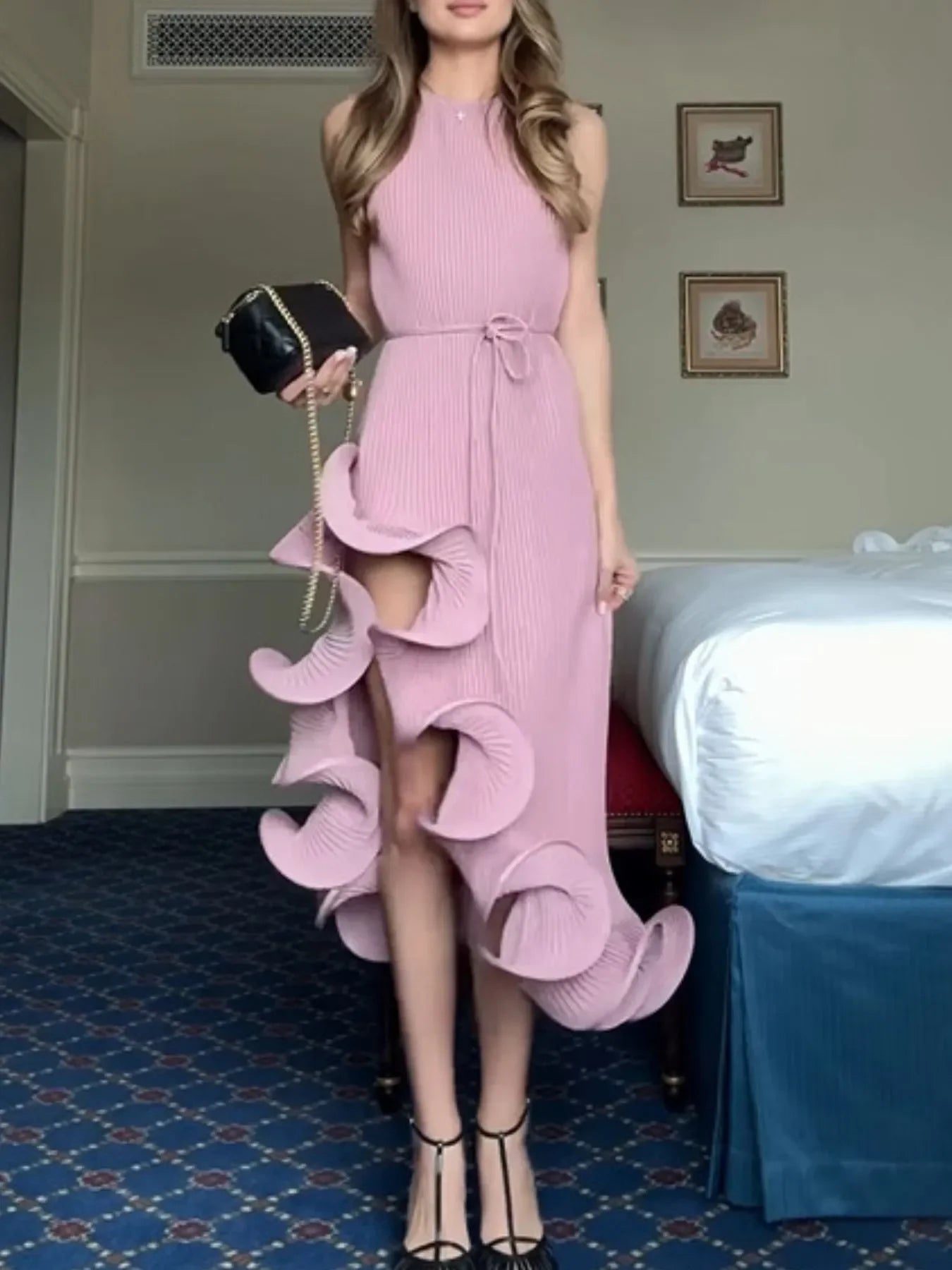 Woman in pink sleeveless ruffle dress with pleated texture, holding black handbag