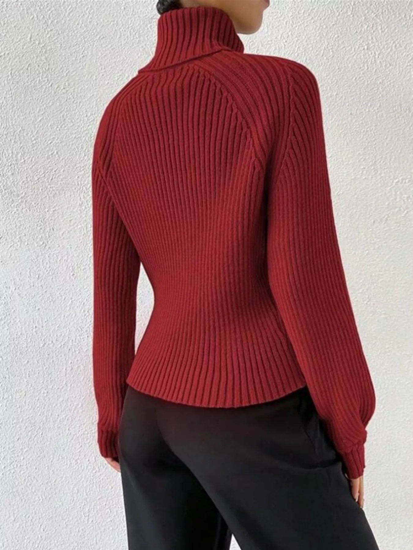 Back view of a woman wearing a red ribbed turtleneck sweater and black trousers.