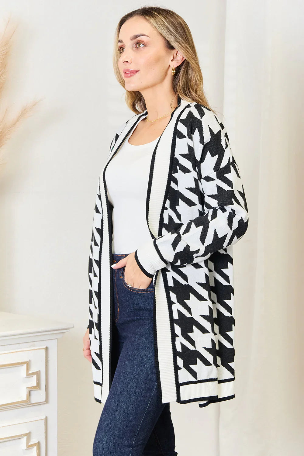 Woman wearing black and white houndstooth knit cardigan with white top and blue jeans indoors