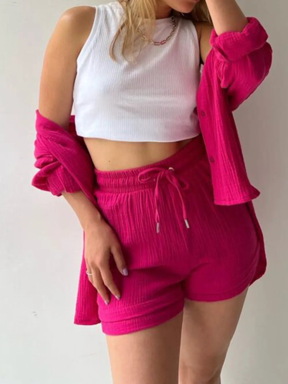 Woman wearing a white crop top and bright pink matching shorts set with overshirt