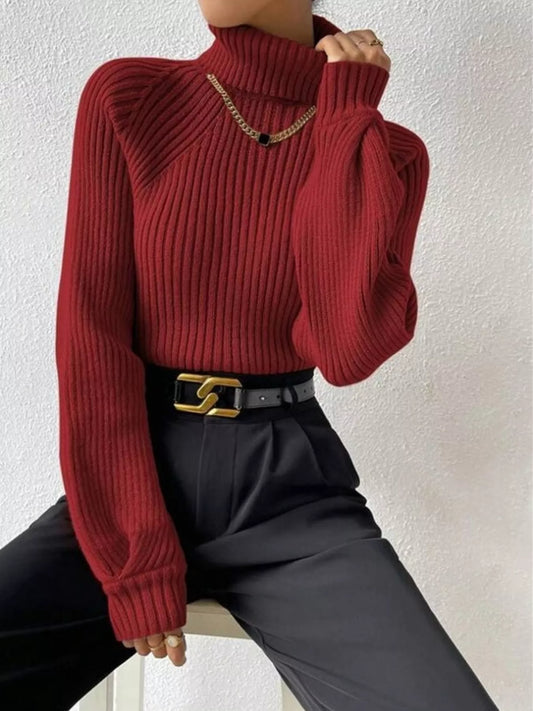 Woman wearing a ribbed red turtleneck sweater, black trousers, and a gold chain necklace.