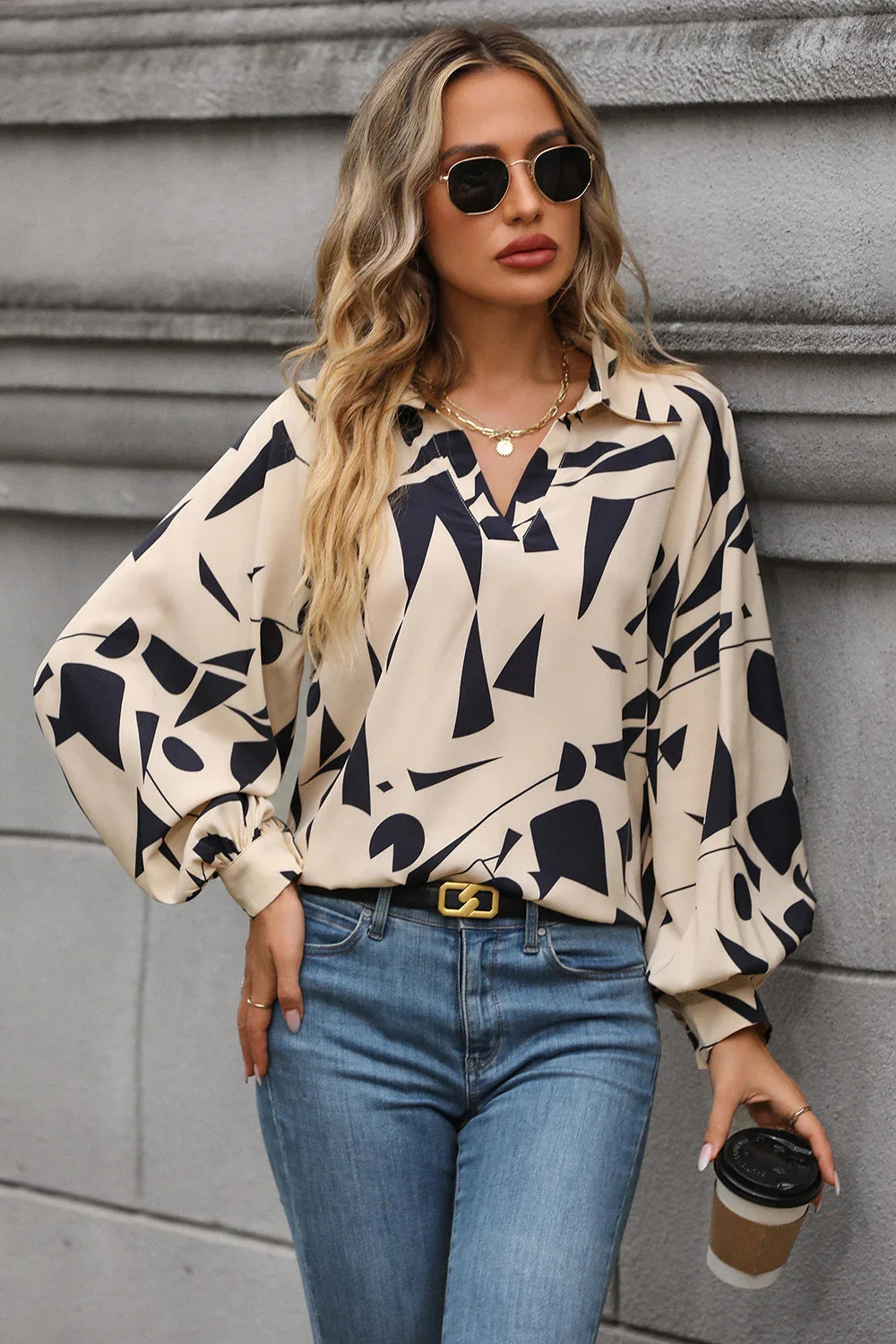 Woman wearing a beige abstract print blouse with long sleeves and blue jeans outdoors