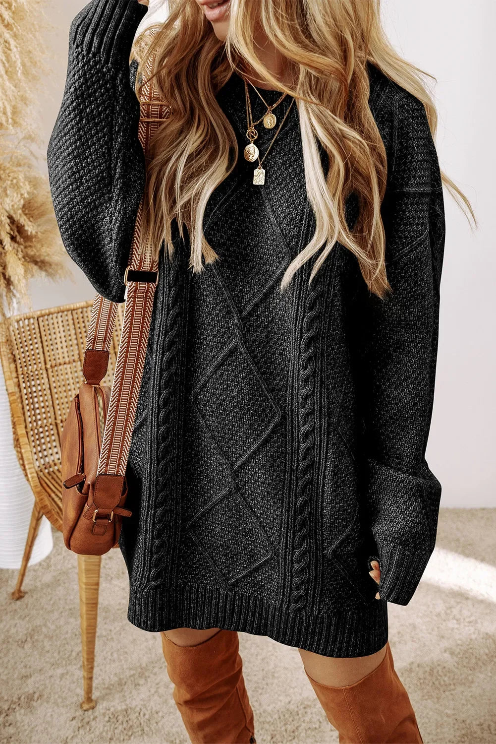 Woman wearing black textured cable knit sweater dress, brown suede boots, and layered gold necklaces