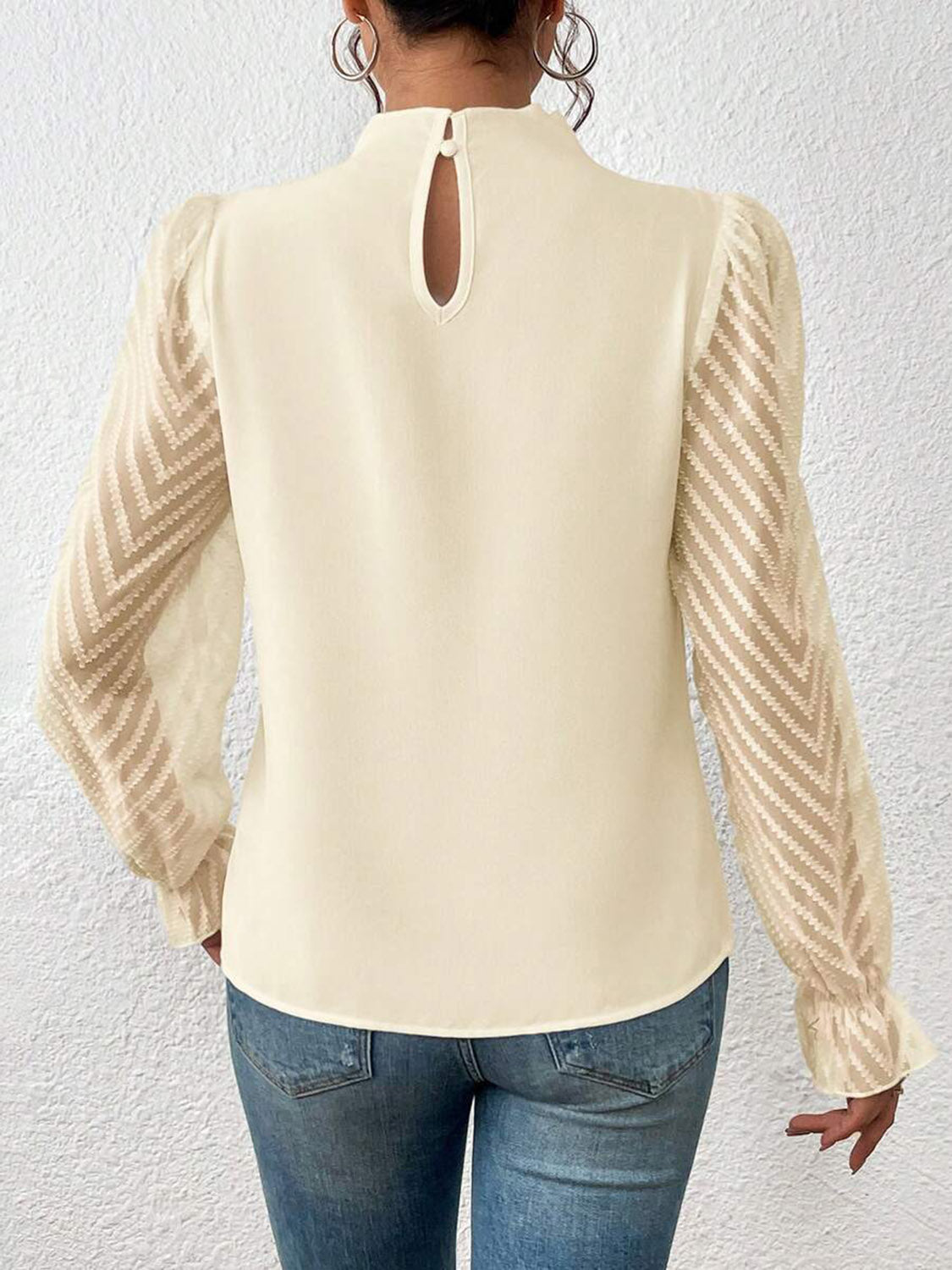 Back view of woman in cream blouse with sheer chevron sleeves and blue jeans