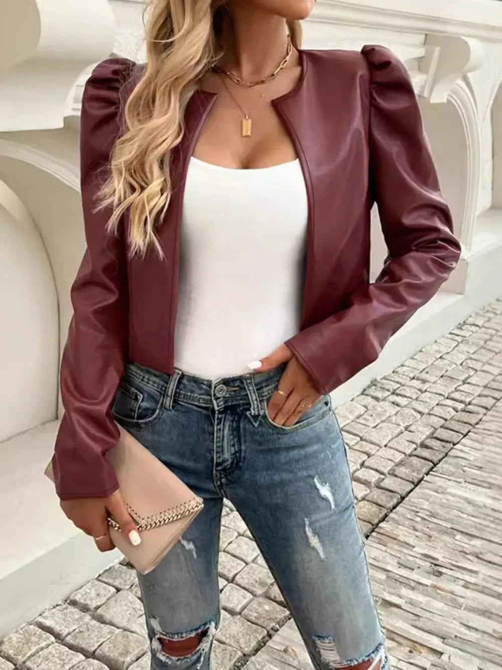 Woman wearing a burgundy faux leather puff sleeve jacket, white top, and distressed blue jeans.
