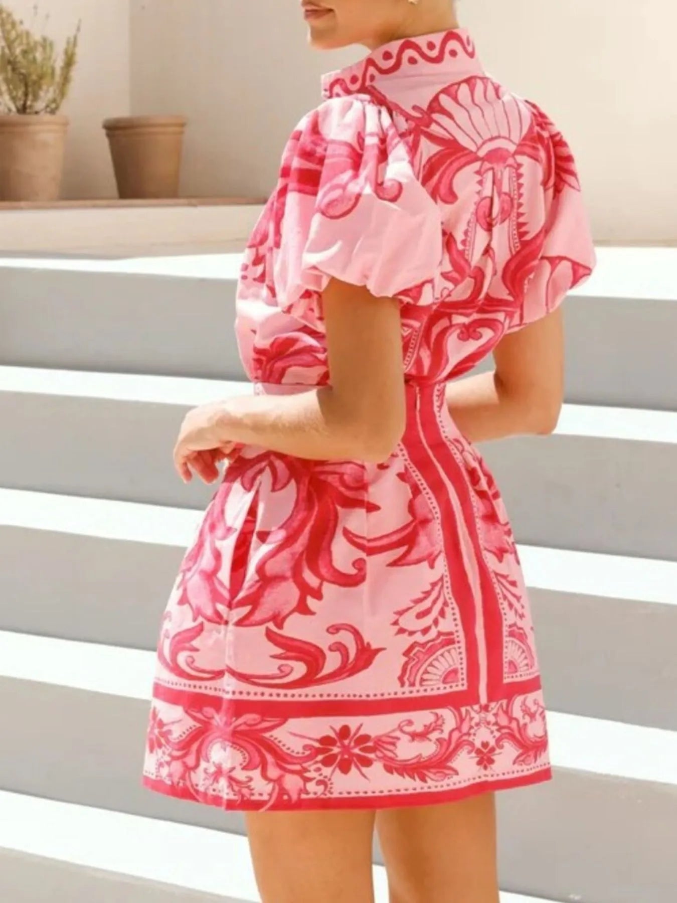 Woman in pink and red patterned mini dress with puff sleeves outdoors
