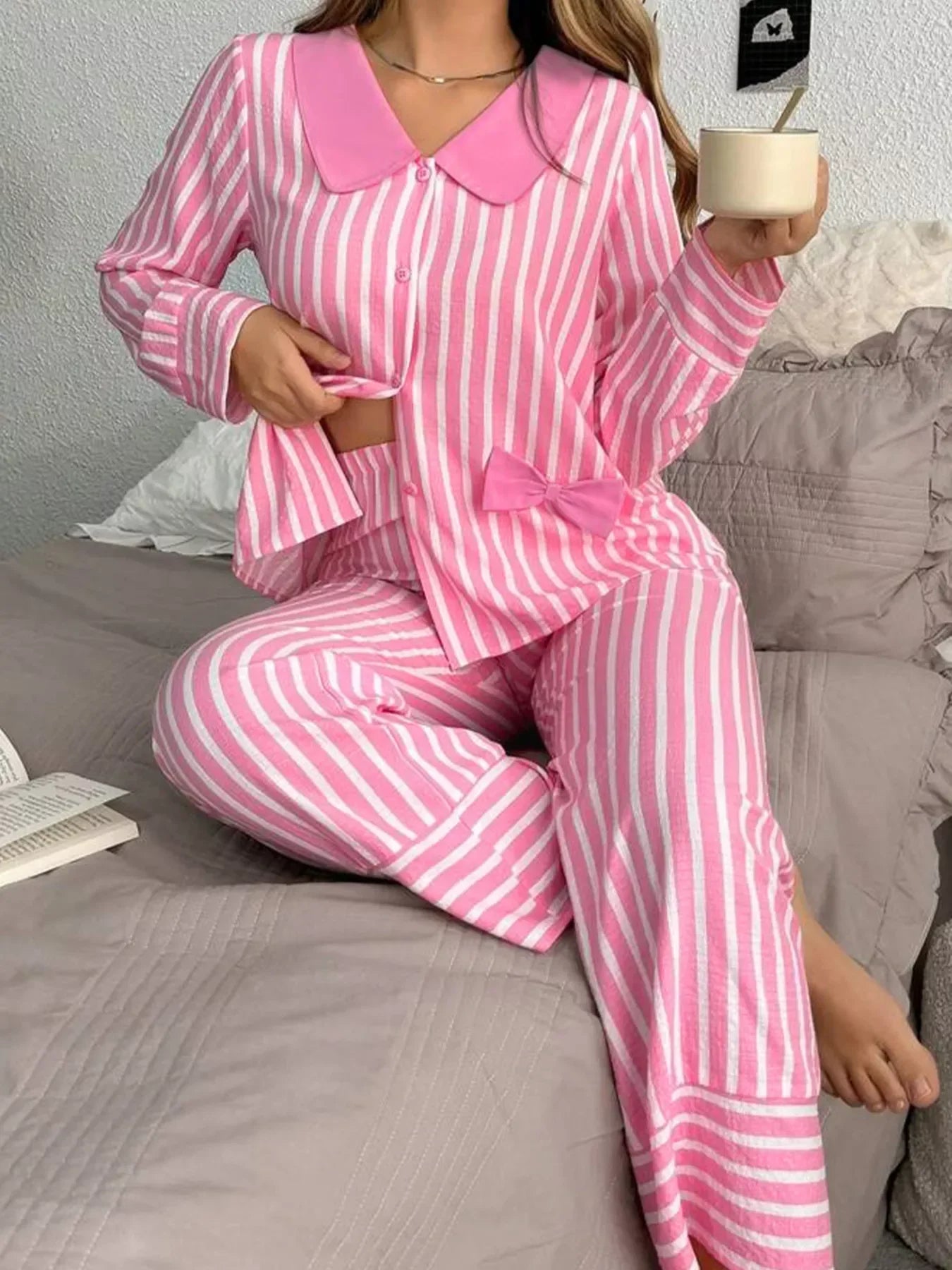 Person wearing pink and white striped pajamas with bow detail, sitting on bed holding a white mug