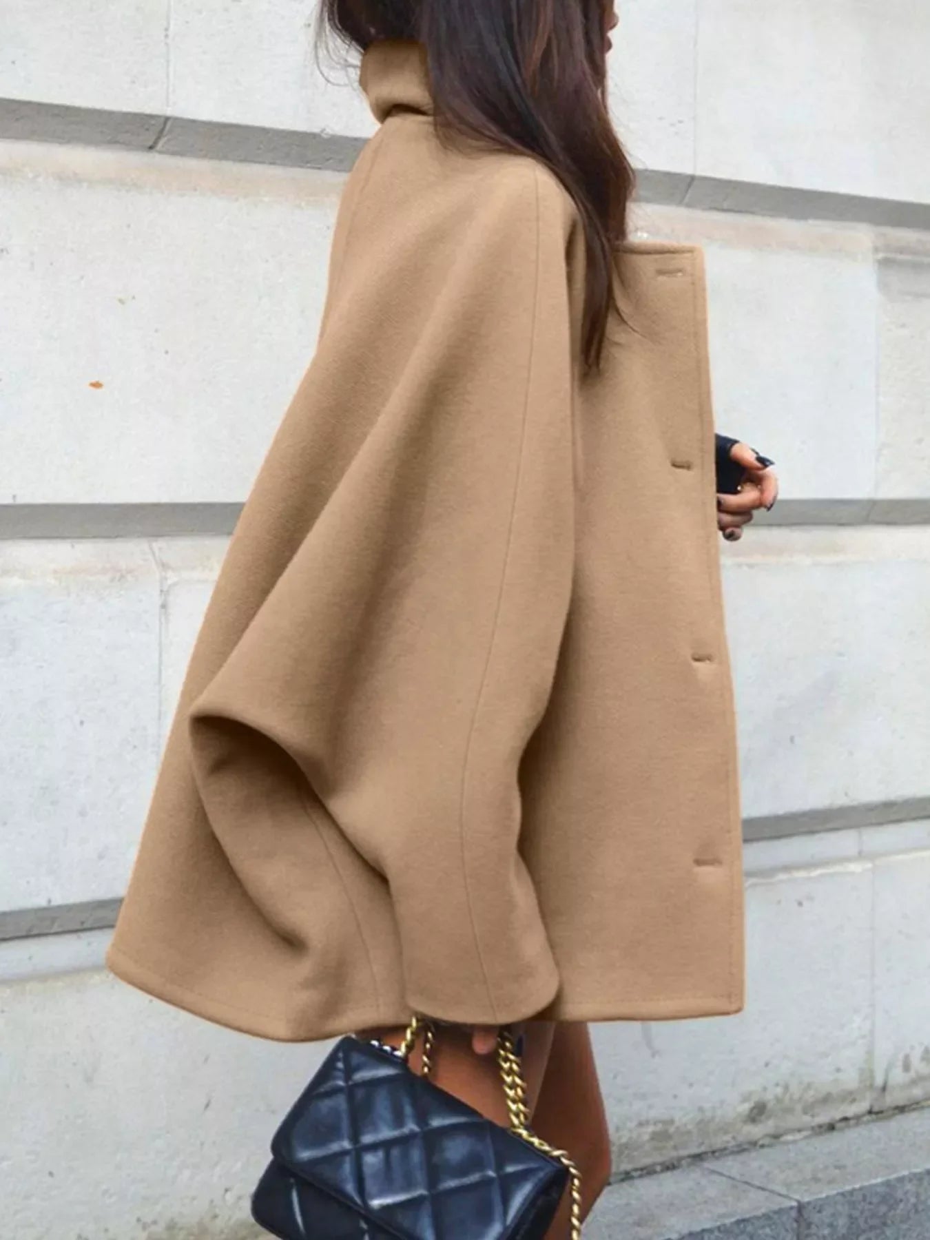 Woman wearing a camel-colored wool cape coat and carrying a black quilted handbag