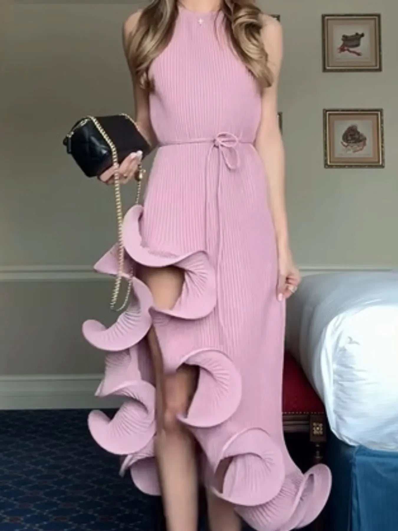 Woman in pink textured ruffle dress holding black purse, modern feminine outfit