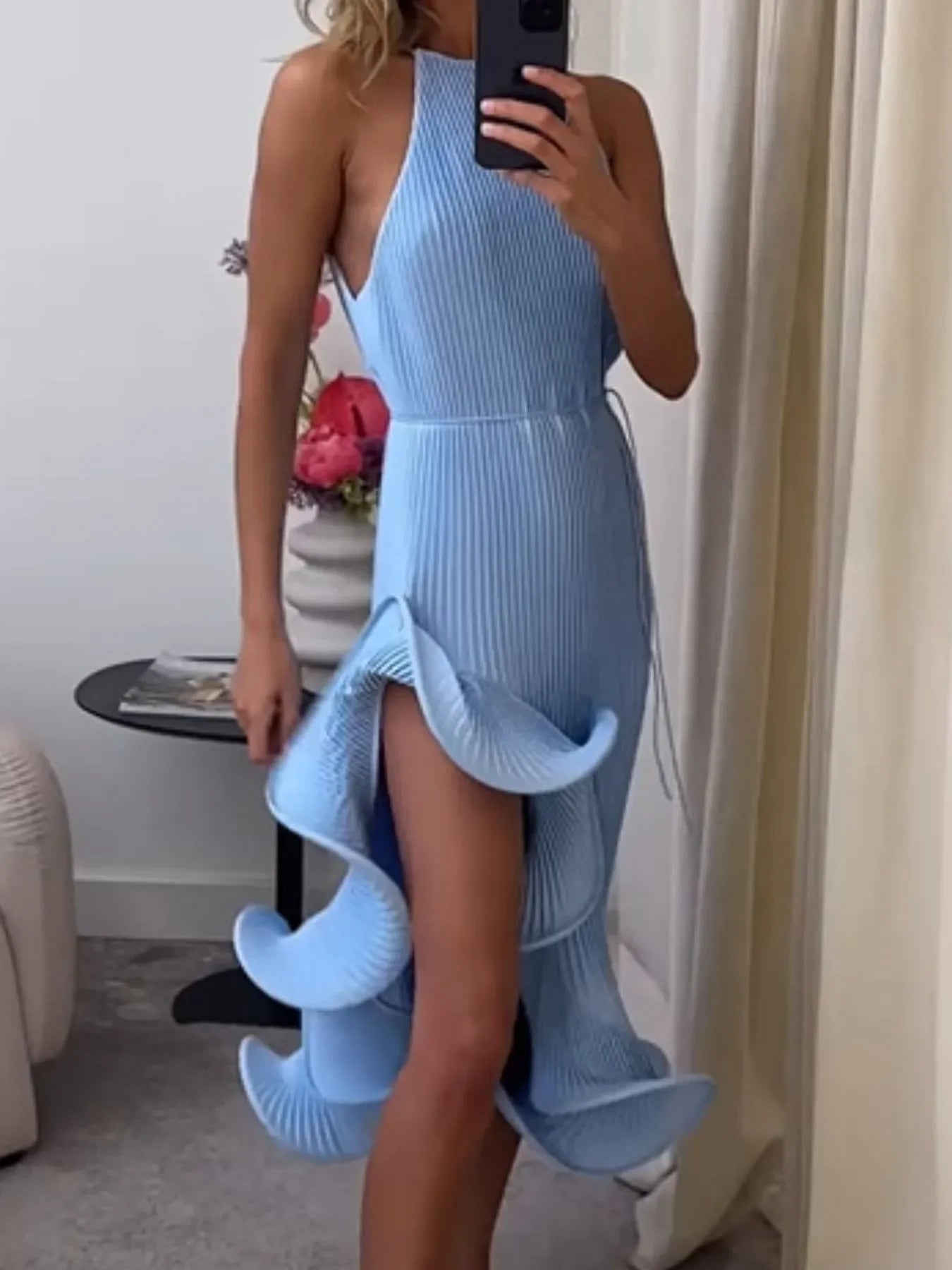 Woman wearing a light blue pleated midi dress with ruffled high slit, stylish modern design