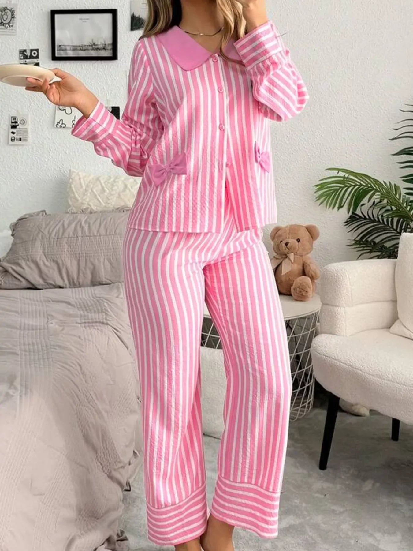 Woman wearing pink and white striped pajamas with bow accents, standing in cozy bedroom setting