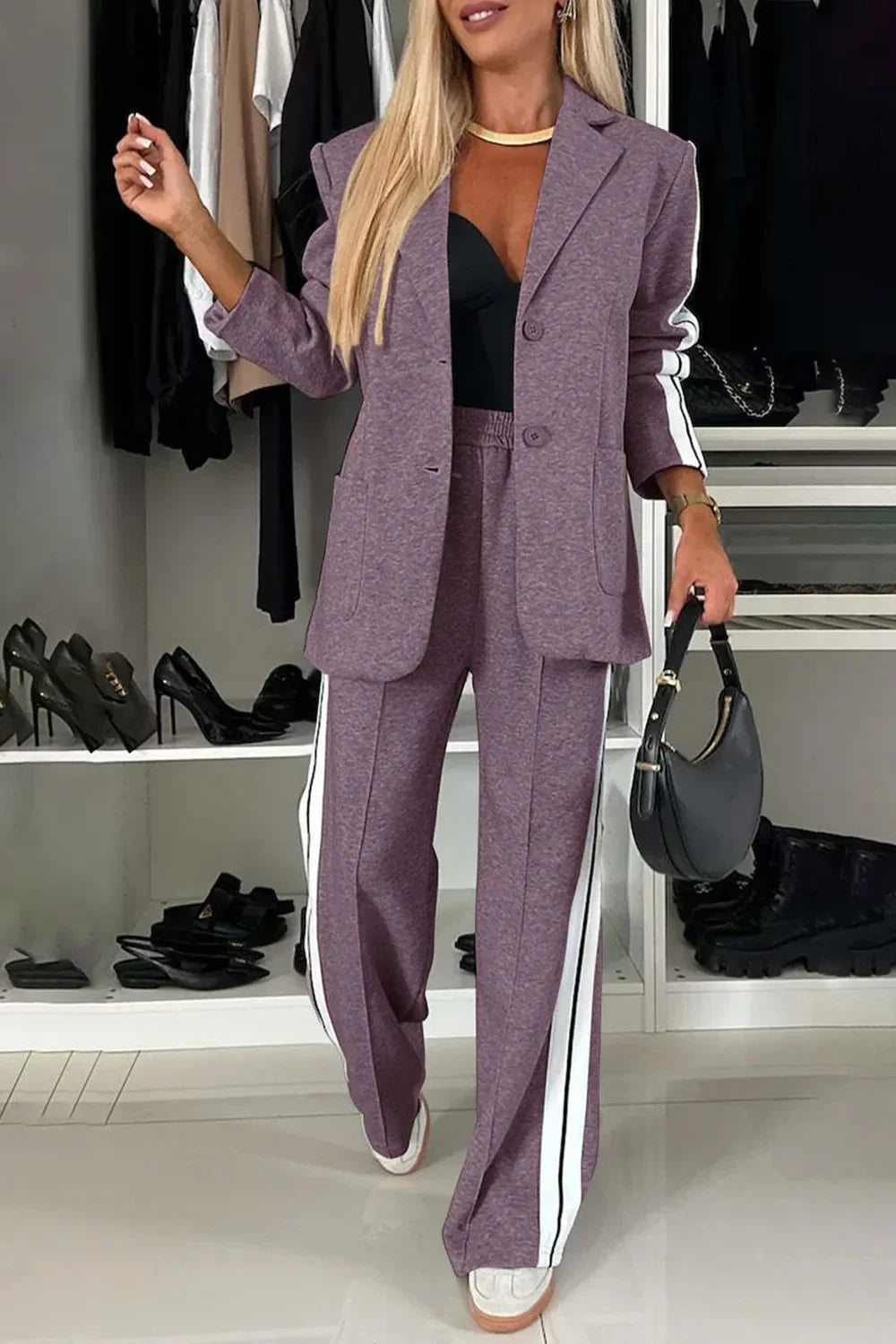 Woman wearing purple sporty blazer and matching wide-leg pants with white stripes, black top, holding black handbag