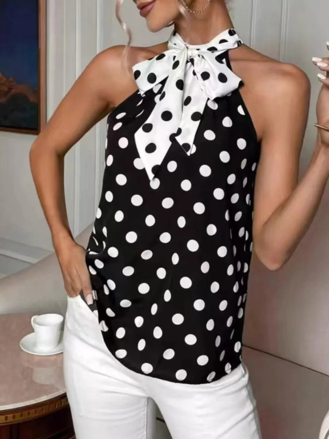 Woman wearing a black and white polka dot halter top with bow detail, paired with white pants.