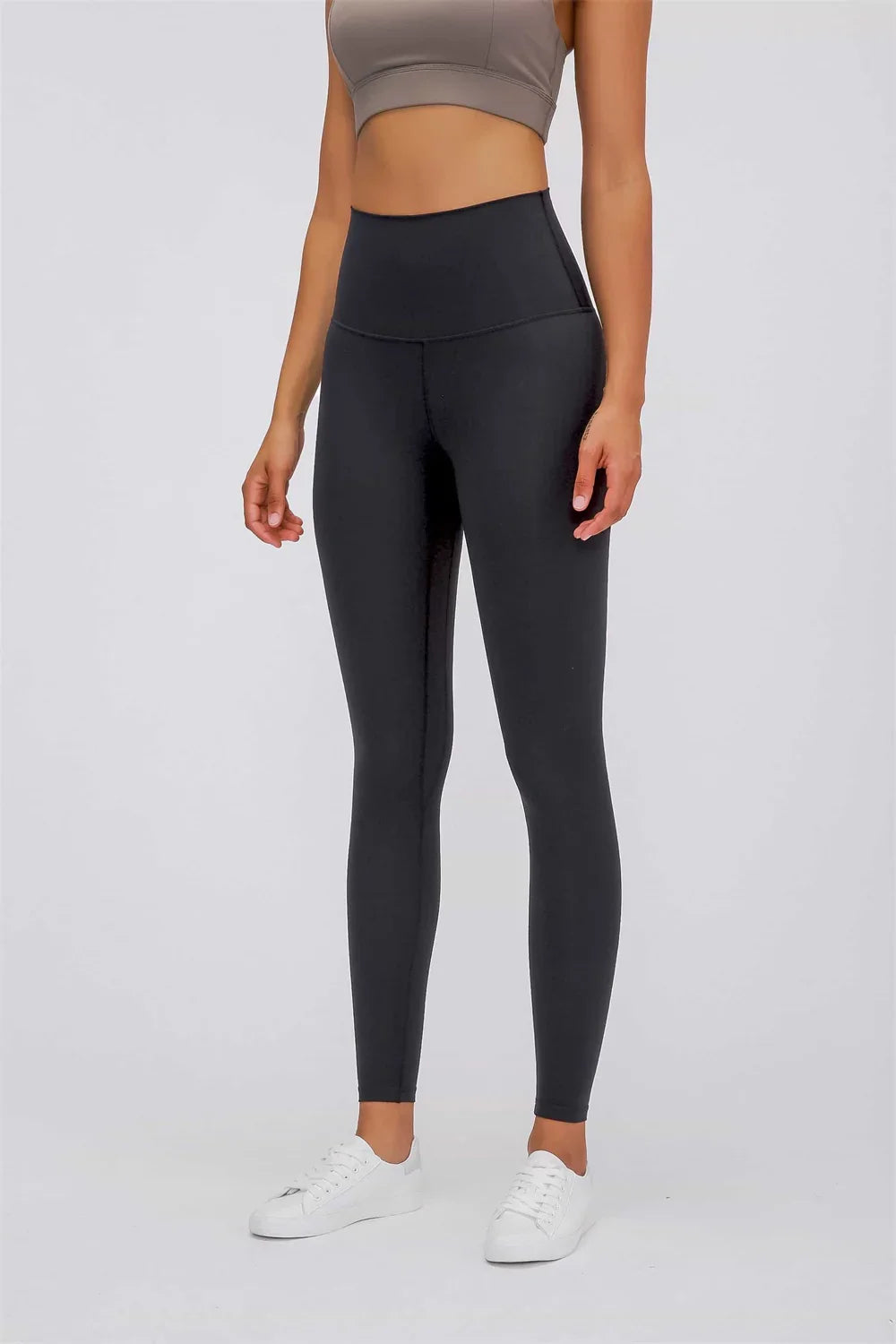 Woman wearing high-waisted black leggings paired with white sneakers and a gray cropped top