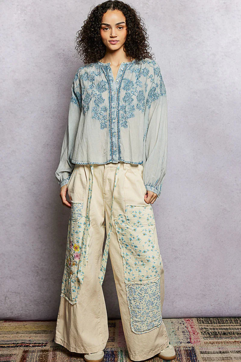 Woman wearing a blue embroidered blouse and cream wide-leg floral patchwork pants