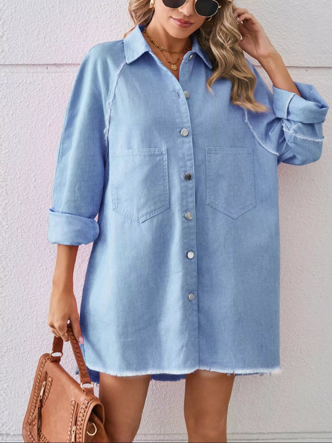 Woman wearing oversized light blue denim button-up shirt dress with brown handbag