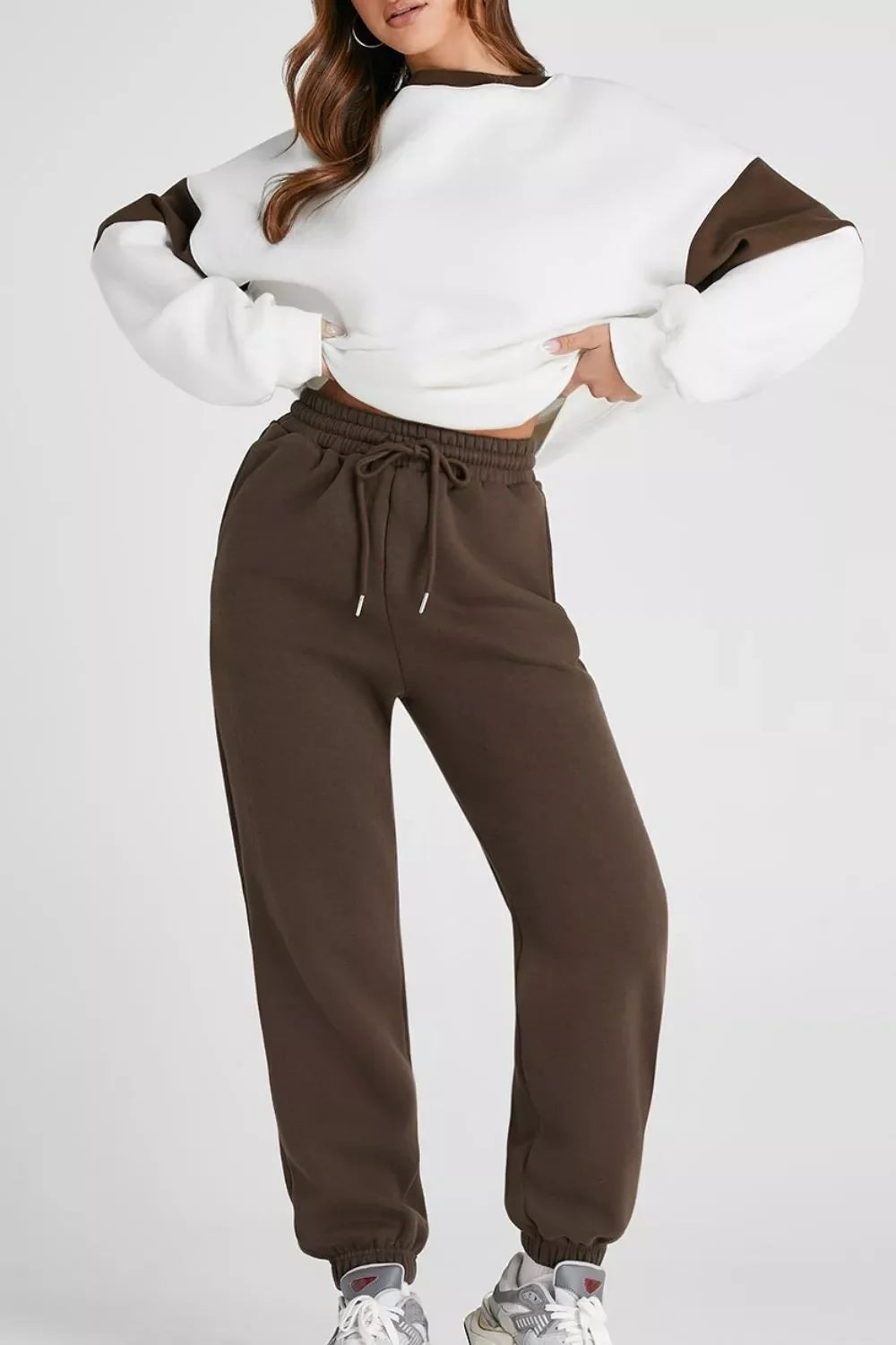 Woman wearing white and brown cropped sweatshirt with brown jogger pants and gray sneakers