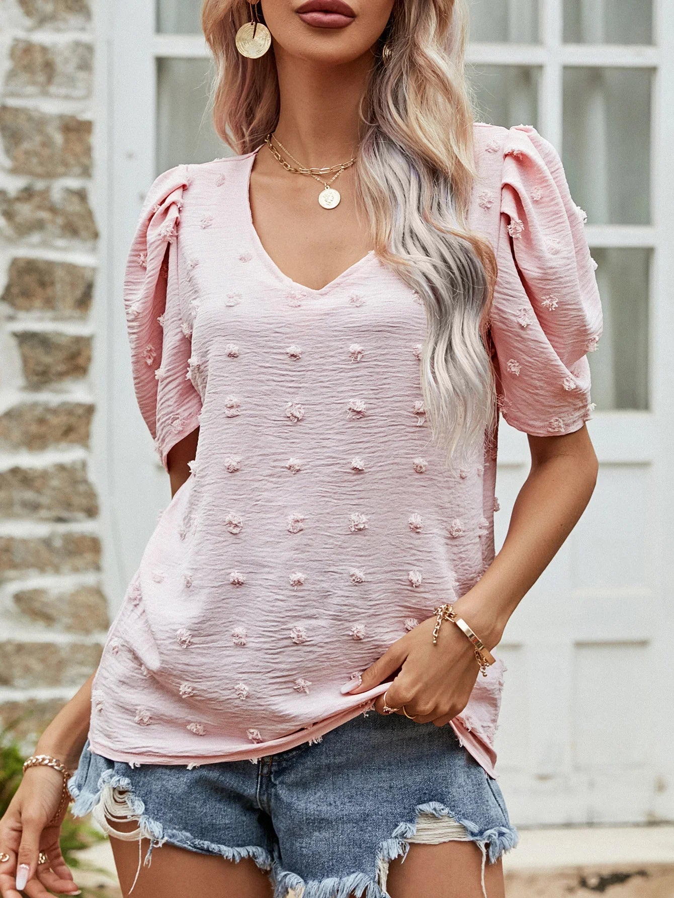 Woman wearing a pink textured puff sleeve blouse with gold jewelry and distressed denim shorts