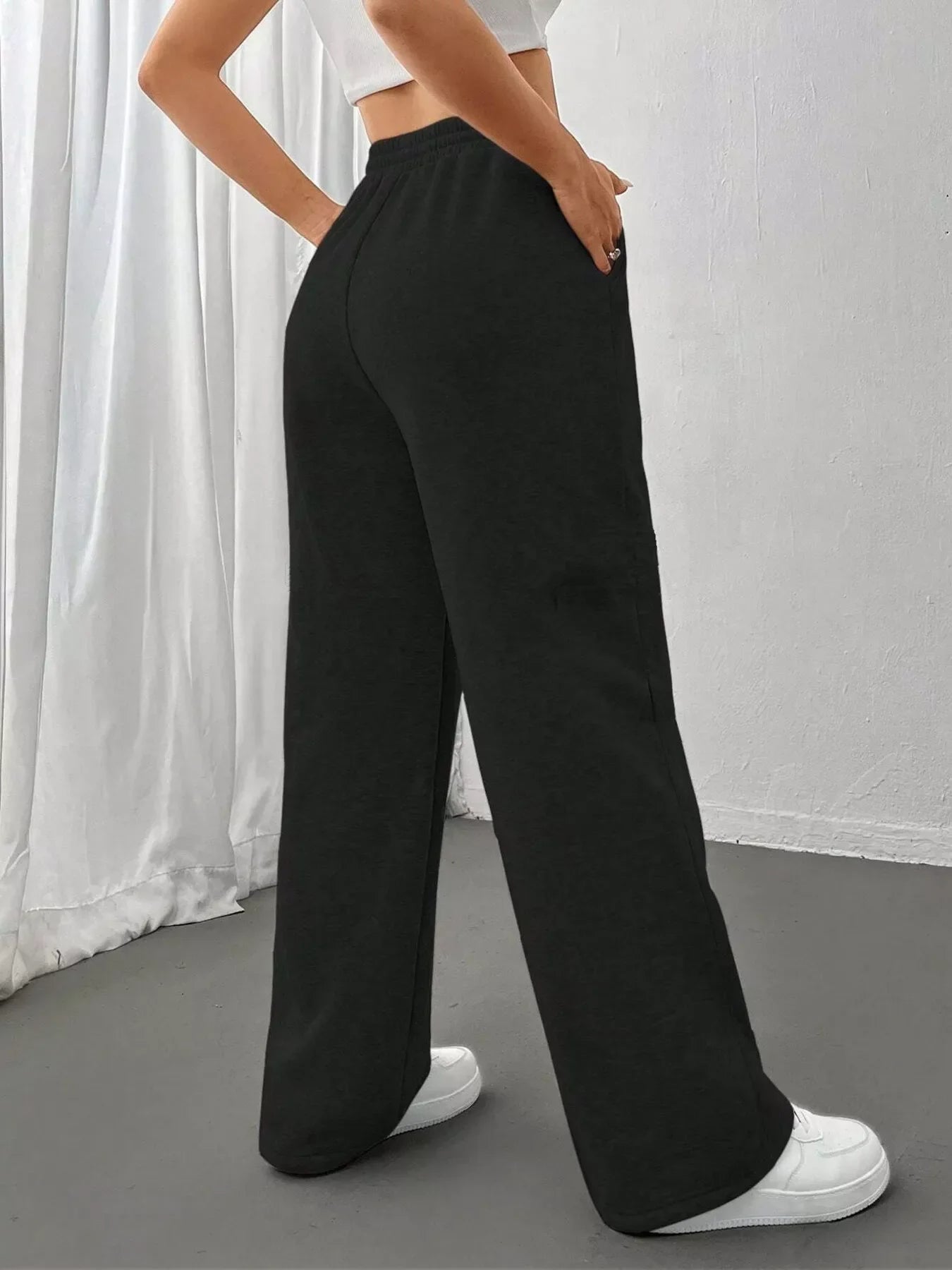 Woman wearing black high-waisted wide-leg pants with white sneakers and a cropped white top