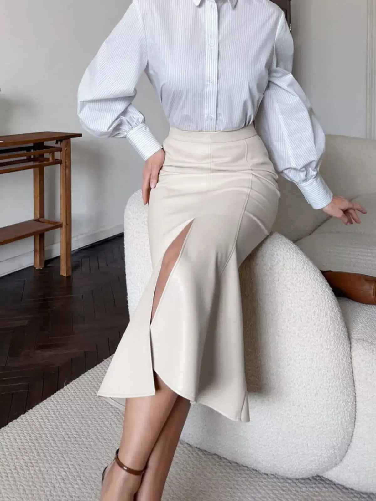 Woman wearing a cream faux leather slit mermaid midi skirt by Evie's Dreamland and a striped blouse.