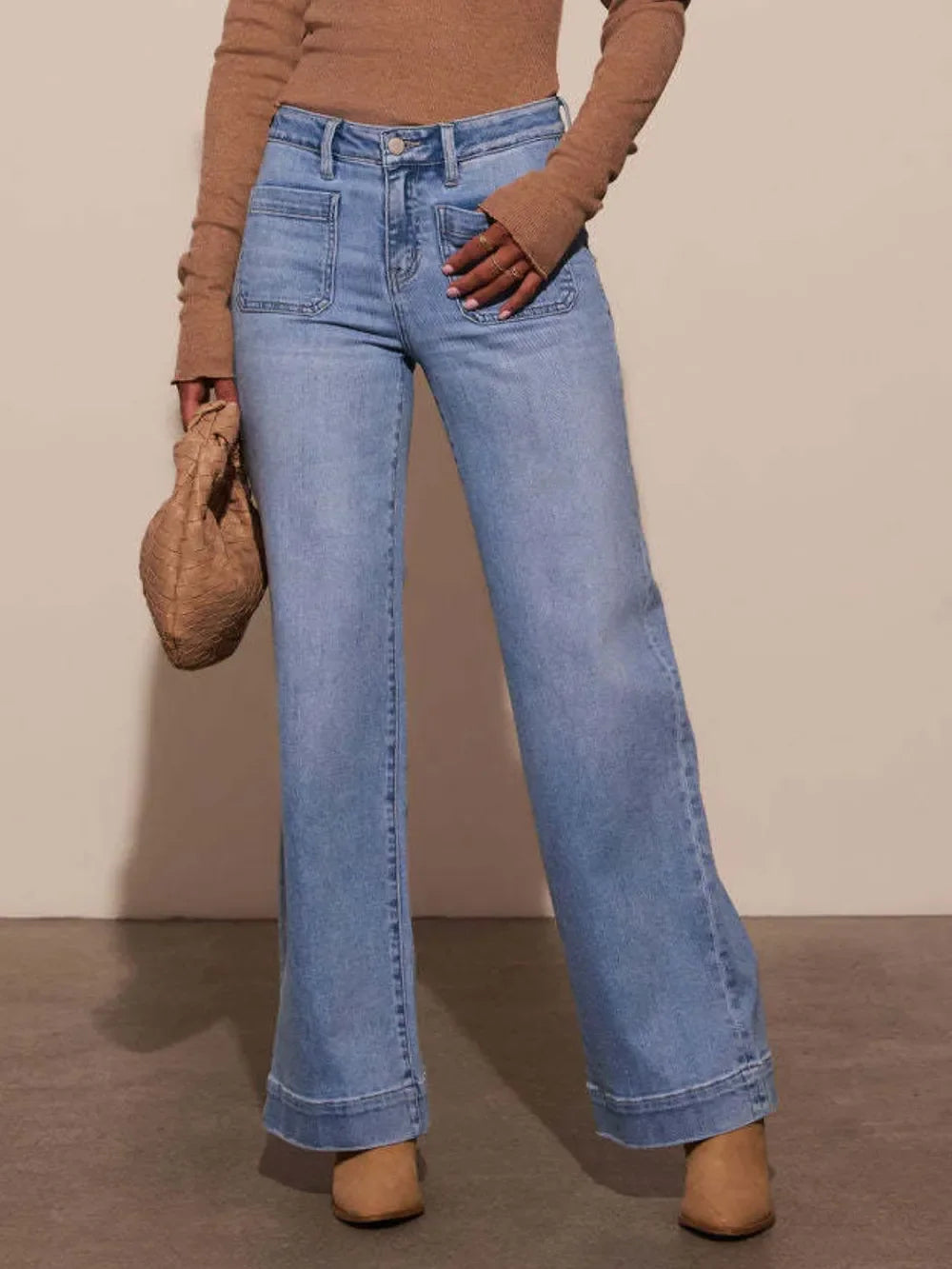 Woman wearing light blue wide leg jeans with front pockets, tan sweater, and beige boots
