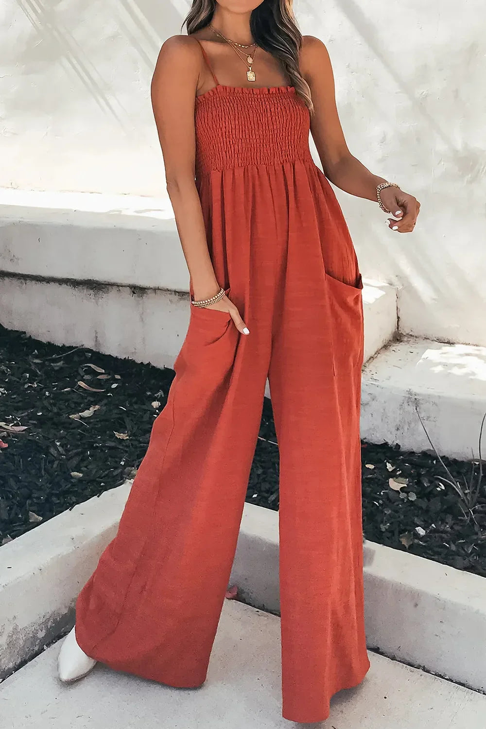 Woman wearing rust orange wide-leg jumpsuit with smocked bodice and pockets outdoors