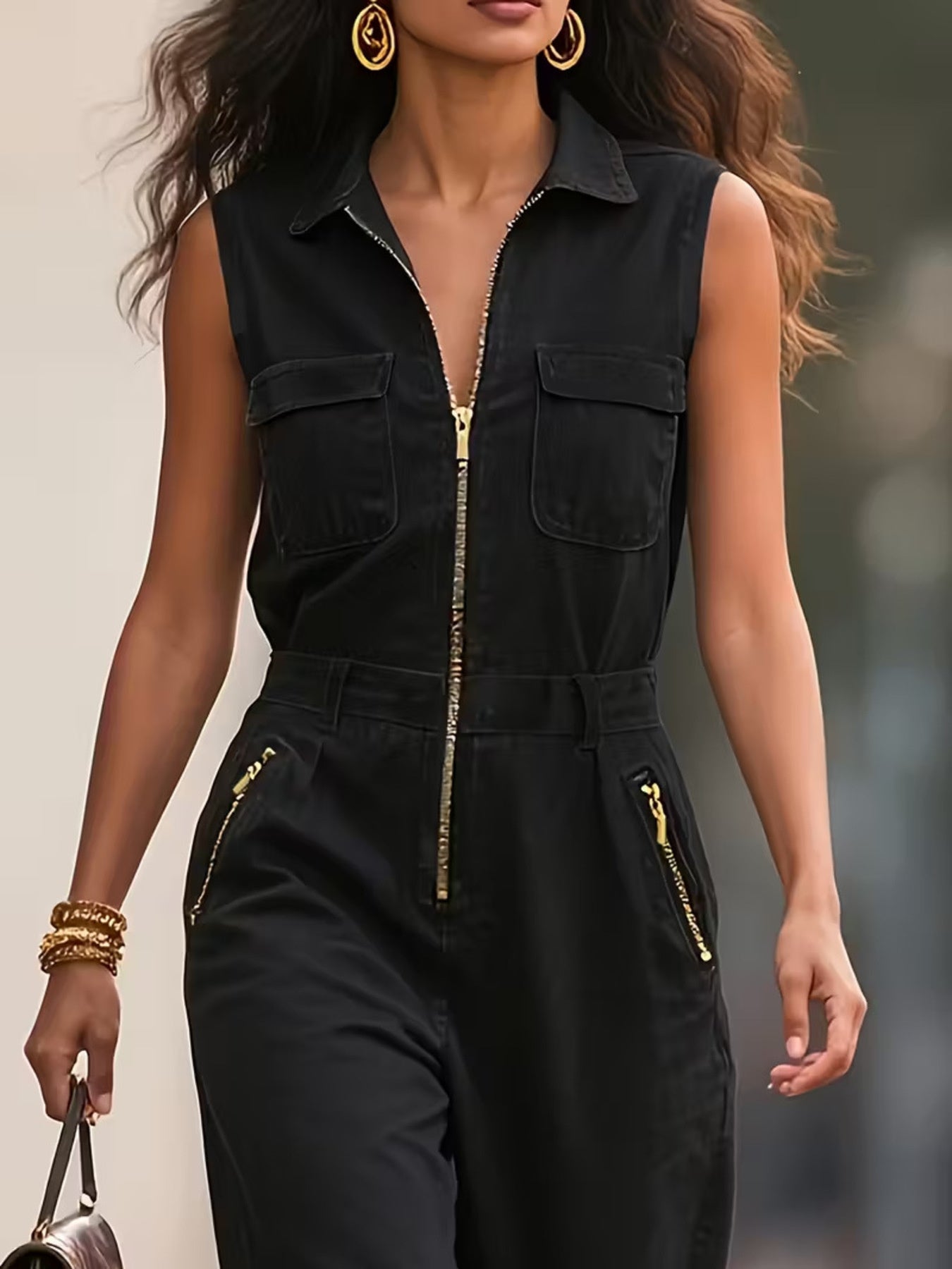 Woman wearing sleeveless black zip-up jumpsuit with gold accents, accessorized with gold jewelry.