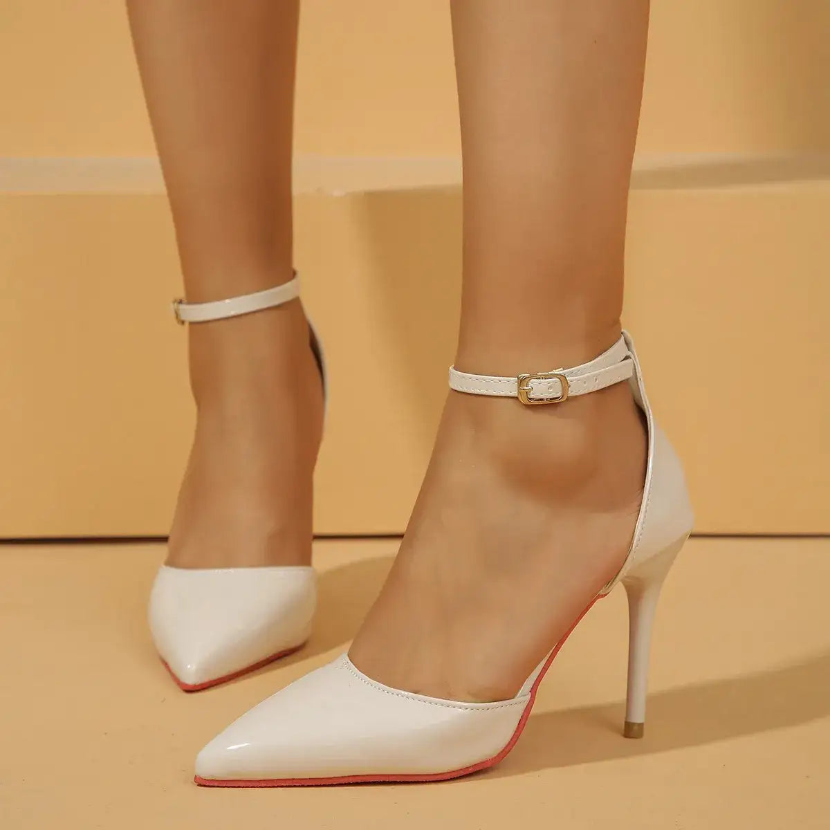 Evie's Dreamland white pointed toe stiletto pumps with gold-buckle ankle straps.