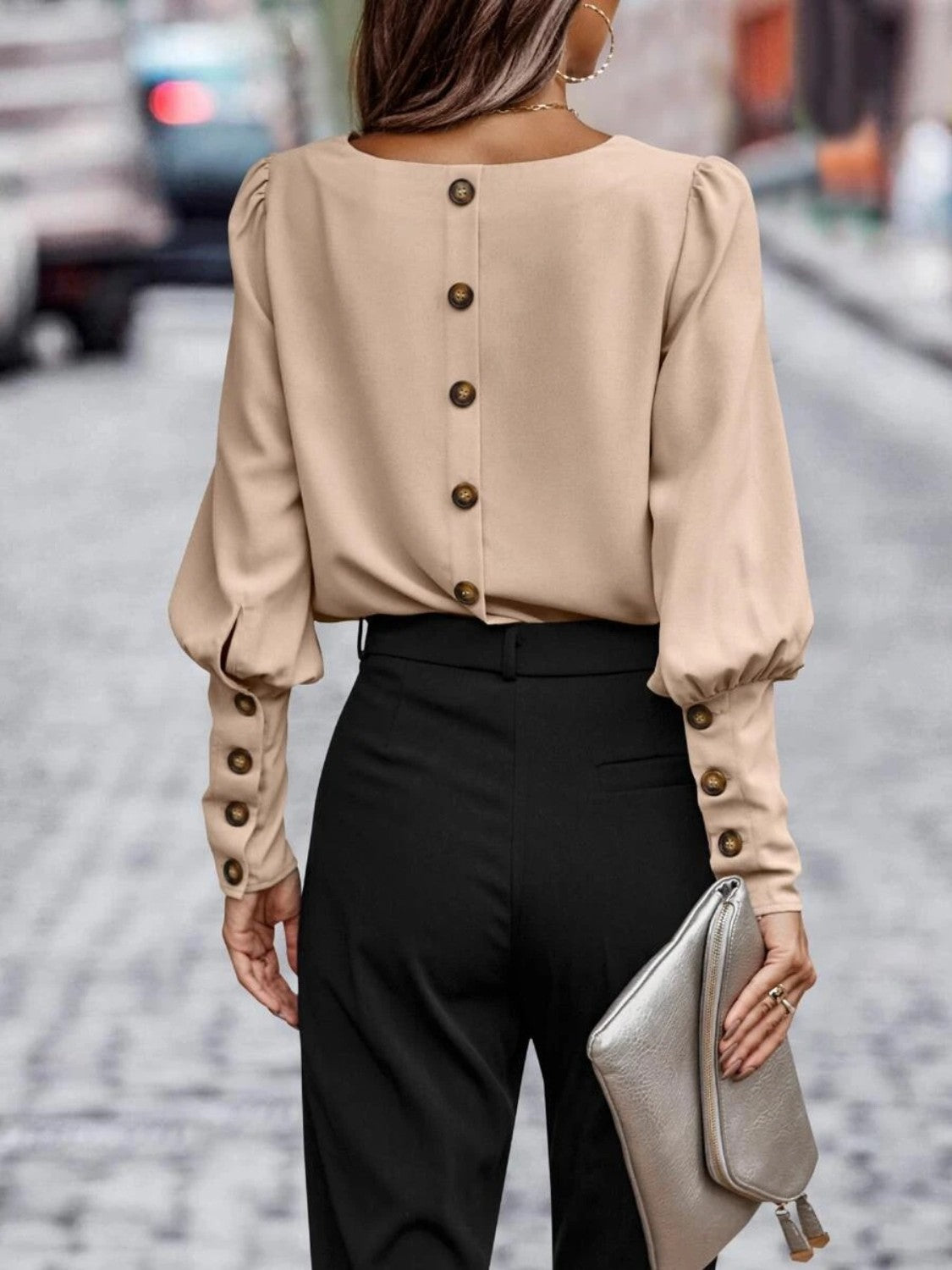 Woman in beige button-back blouse with long sleeves, black pants, holding silver clutch