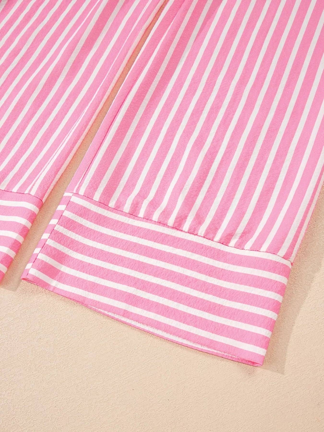 Pink and white vertical striped fabric with a horizontal striped cuff detail on beige surface