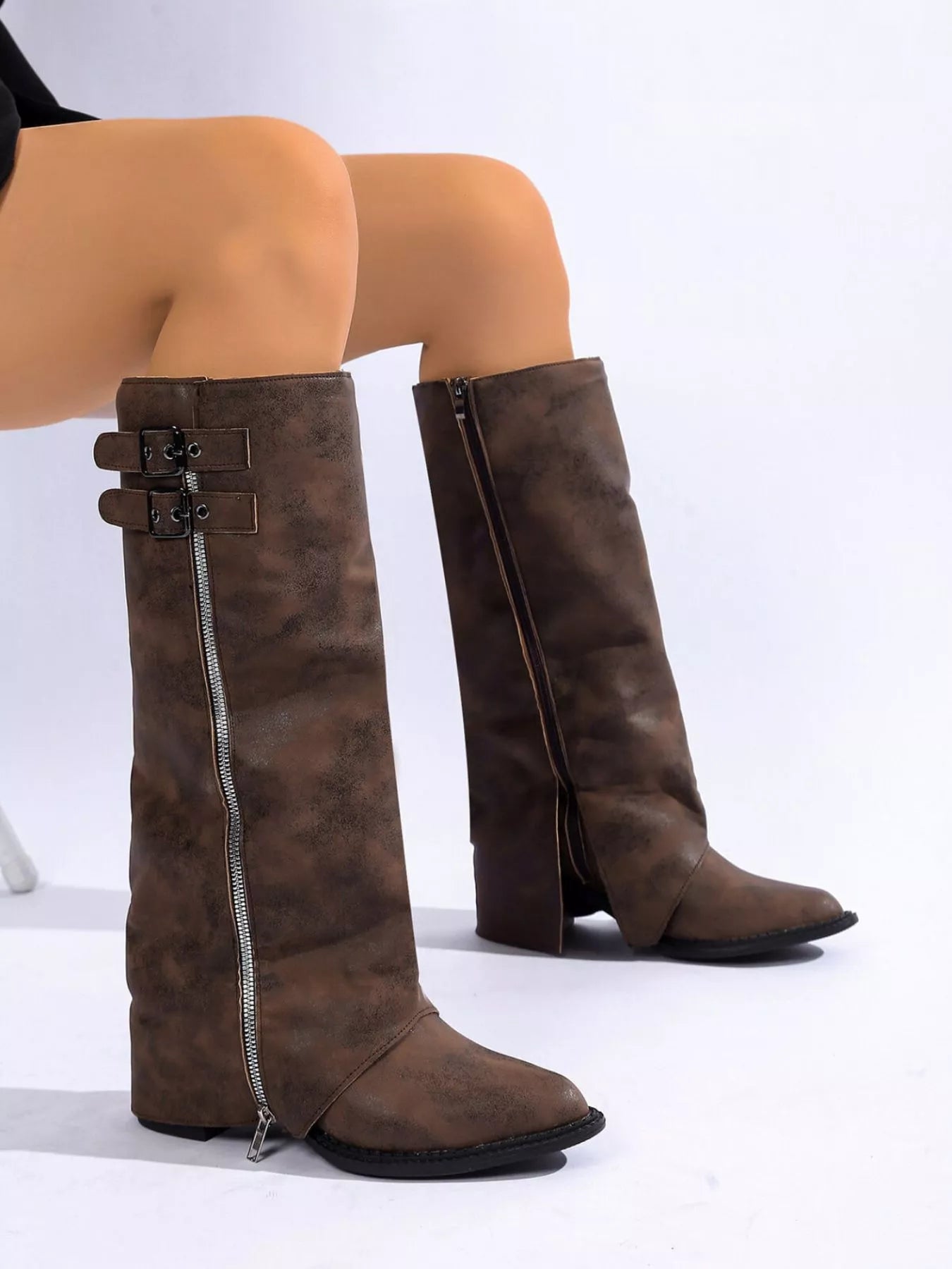 Woman wearing brown faux leather knee-high boots with side zippers and buckle details