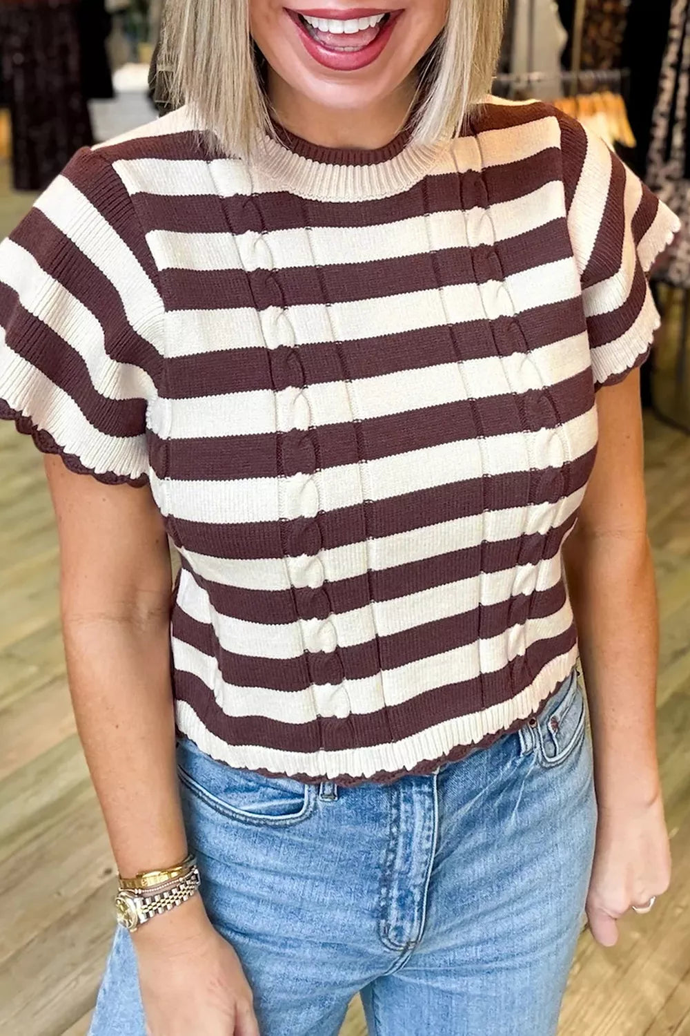Woman wearing a brown and cream striped ribbed cable-knit short sleeve sweater paired with blue jeans.