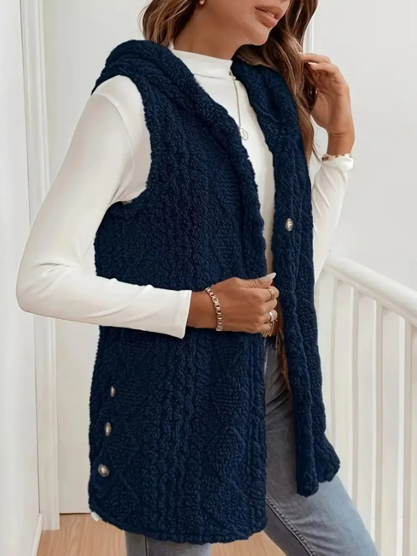 Woman wearing navy blue sherpa fleece vest with side buttons over white long sleeve top and jeans
