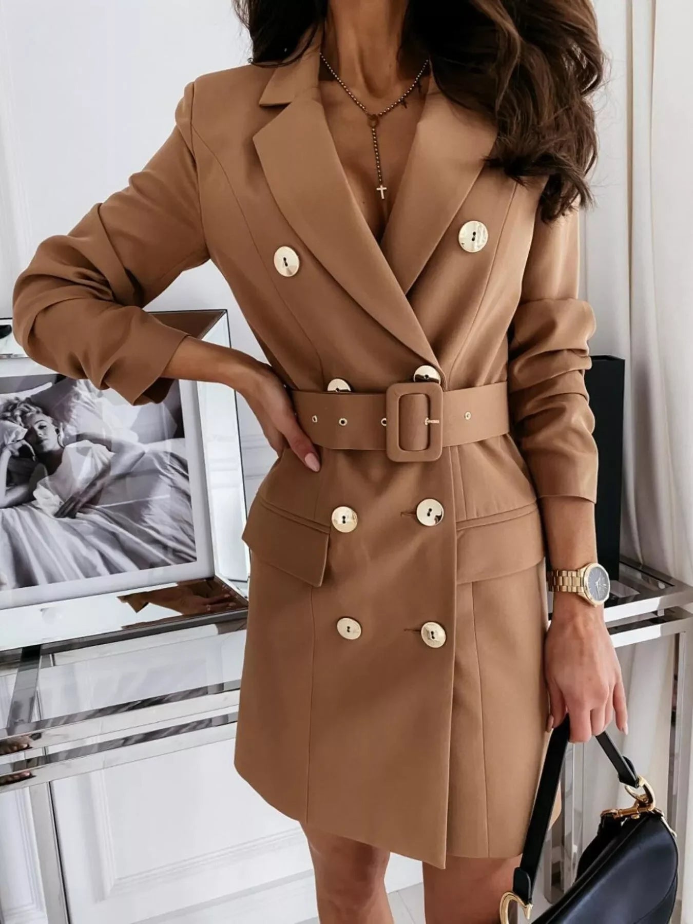 Woman wearing a stylish camel double-breasted blazer dress with a belt, gold watch, and black handbag