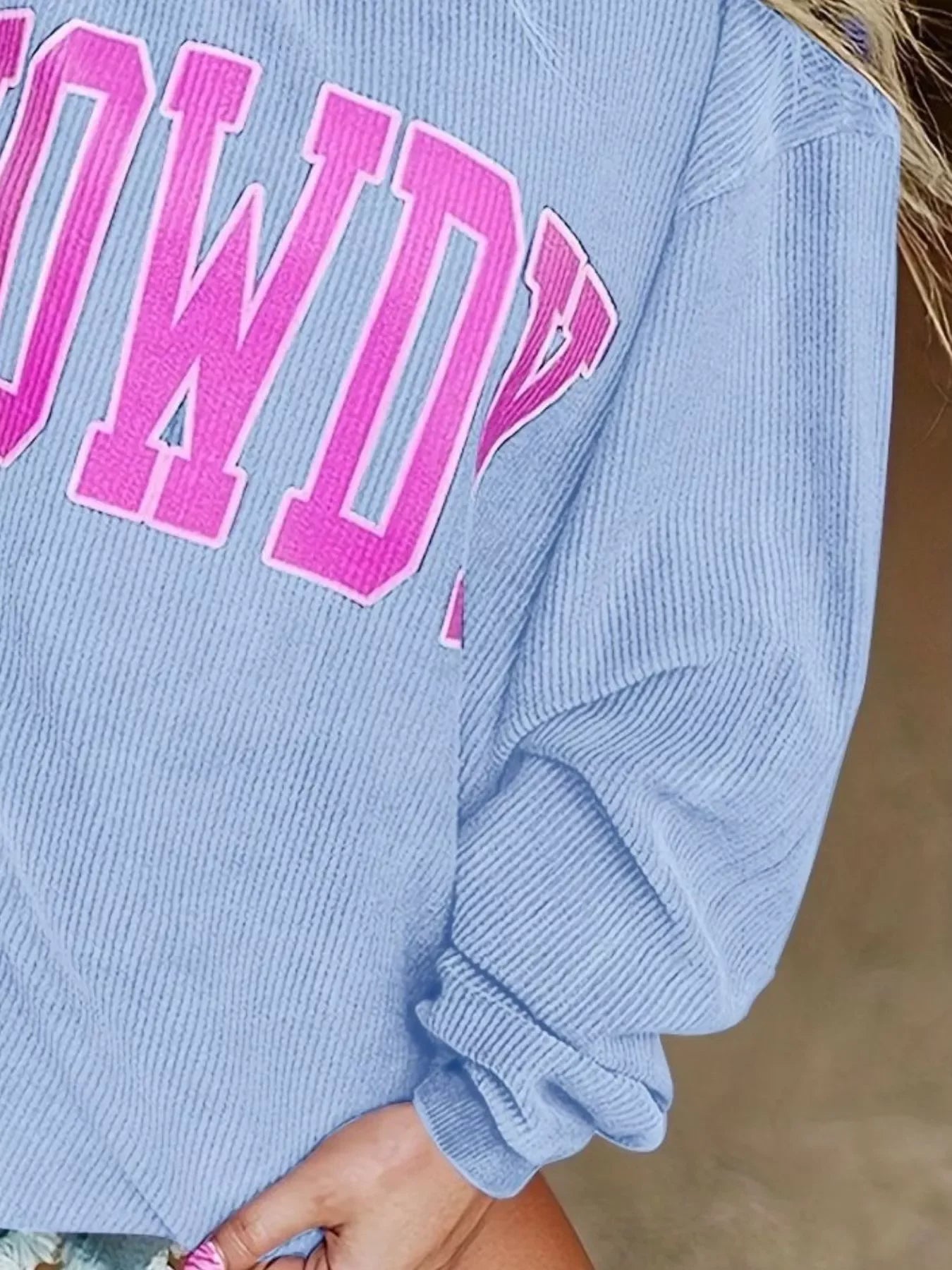 Close-up of light blue ribbed sweatshirt with pink 'ROADWAY' lettering and rolled sleeve