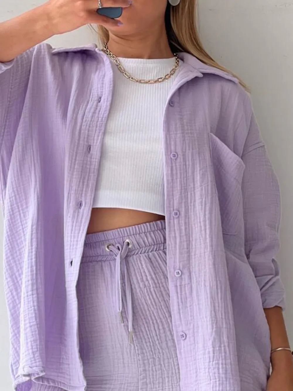 Woman wearing a light purple button-up lounge set with drawstring pants and white crop top
