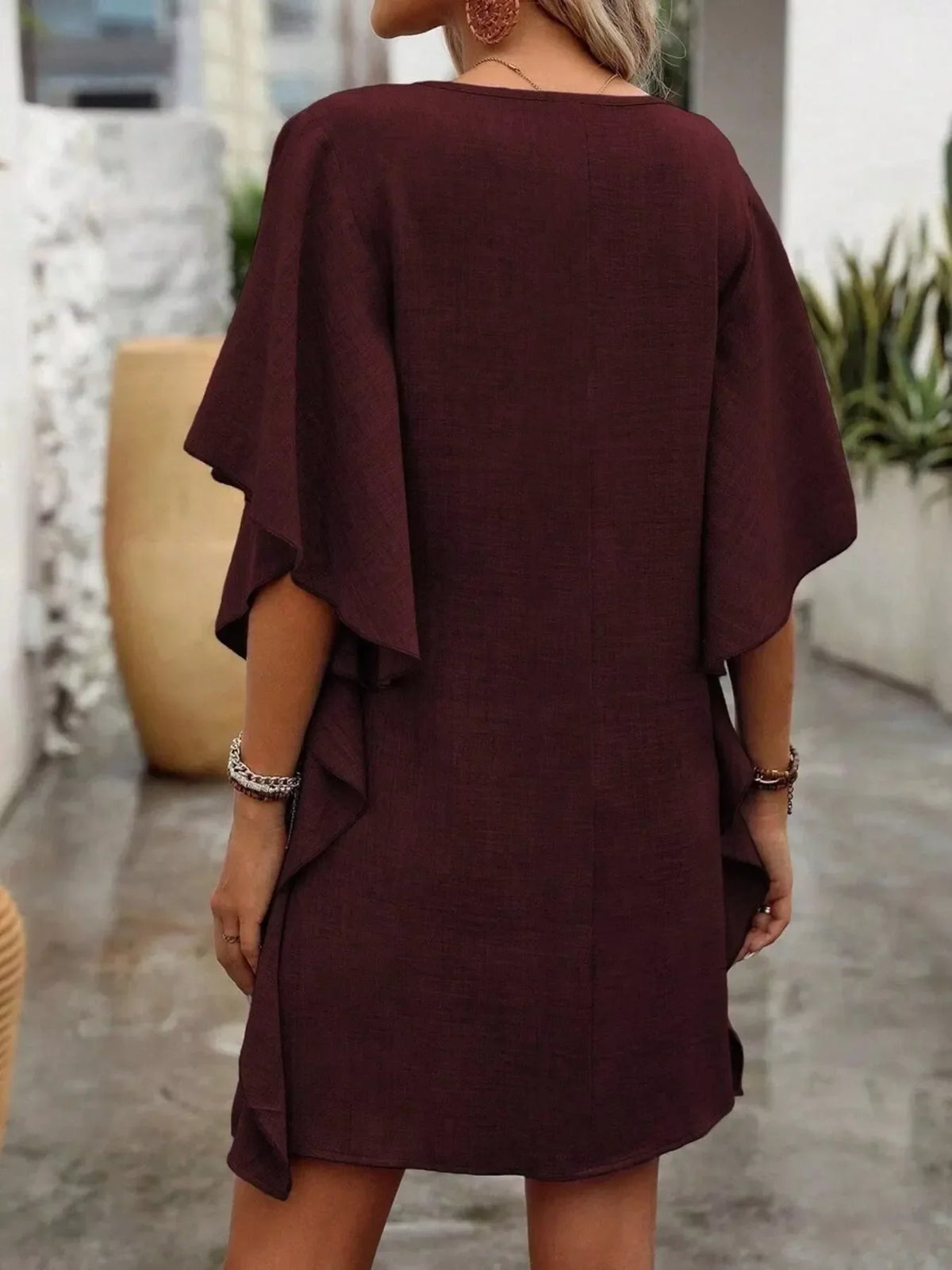 Woman wearing a loose-fit maroon mini dress with flutter sleeves, stylish outdoor setting