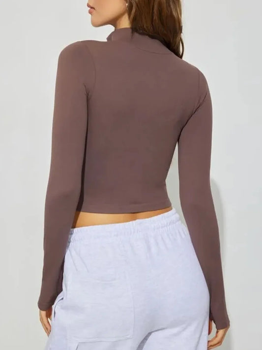 Woman wearing a fitted brown long sleeve crop top and light gray sweatpants, back view