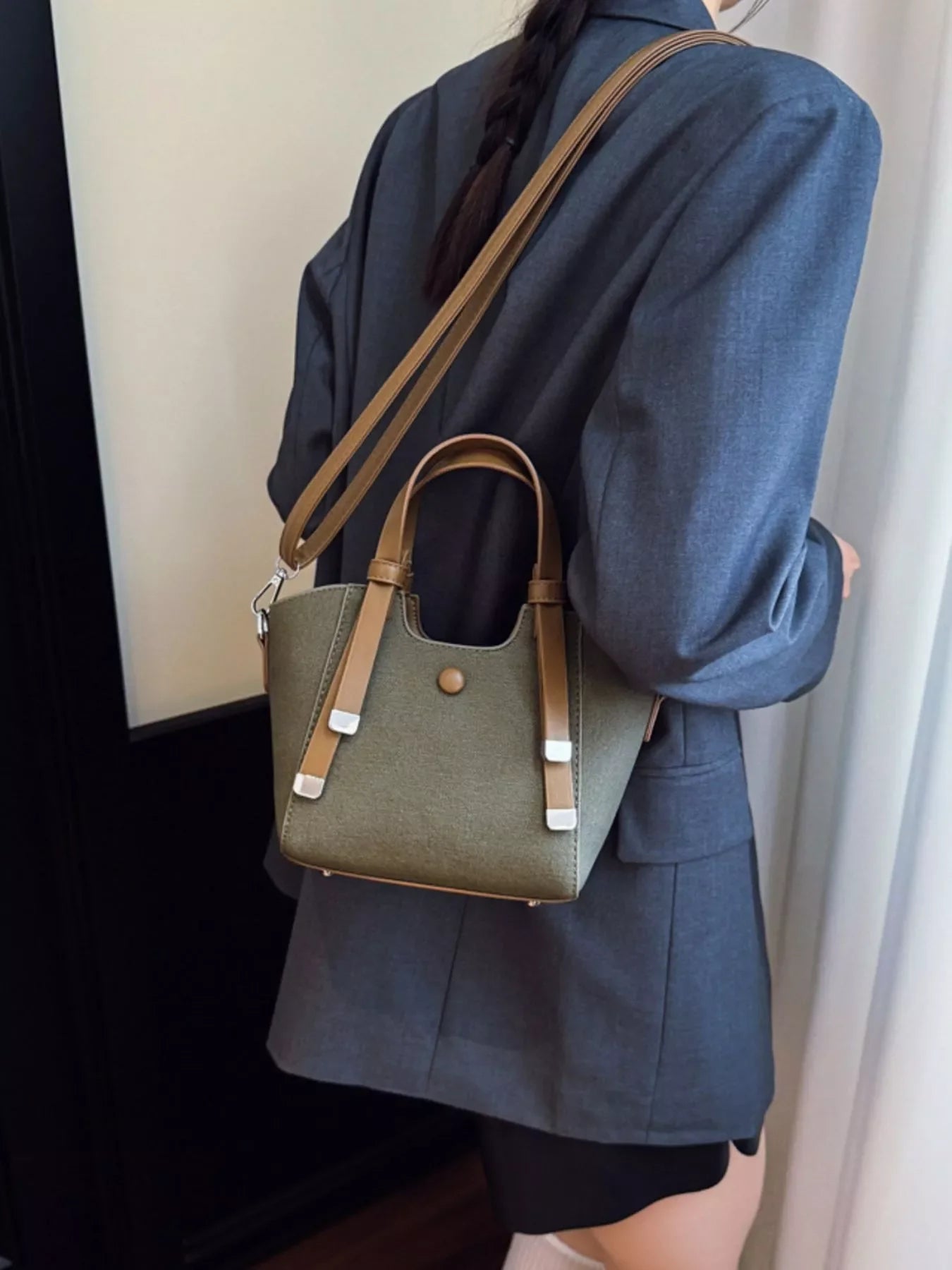 Woman wearing dark blazer carrying stylish small olive green and tan leather handbag with detachable strap
