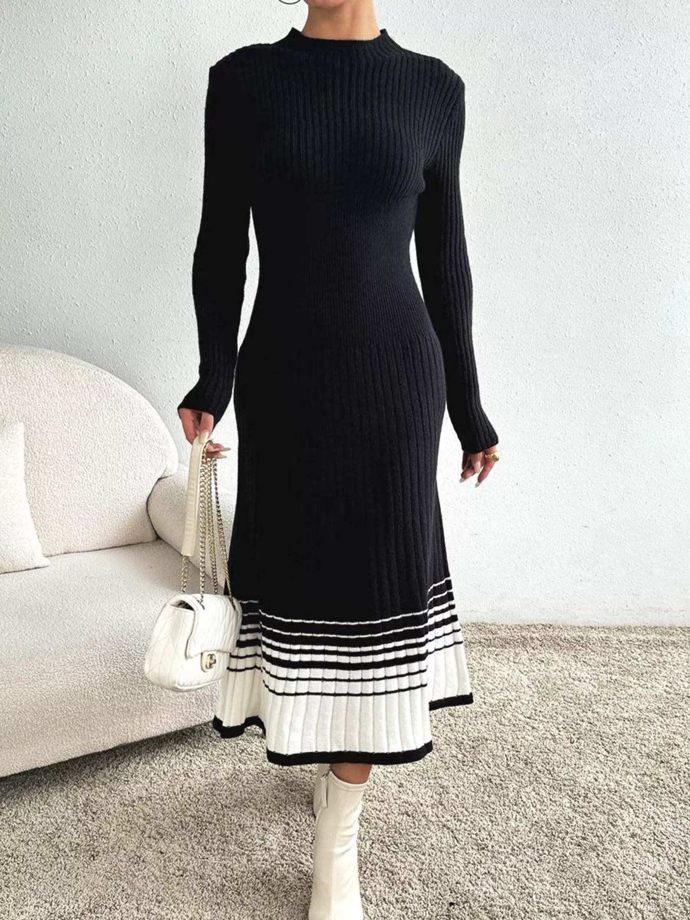 Woman wearing a black ribbed knit midi dress with white striped hem and white boots.